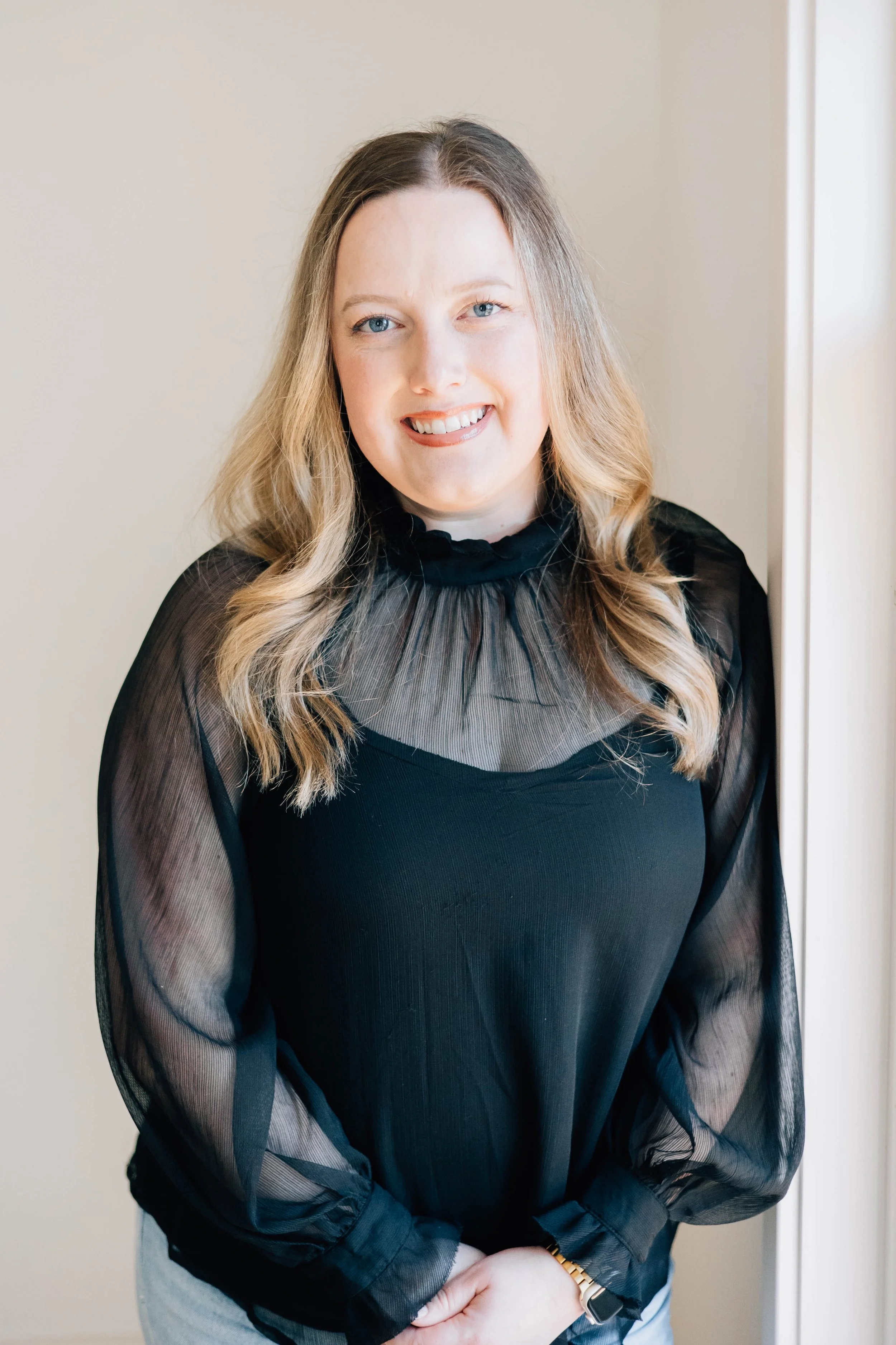 Photo of a woman with medium to long curled blonde hair, wearing a black long sleeve blouse.