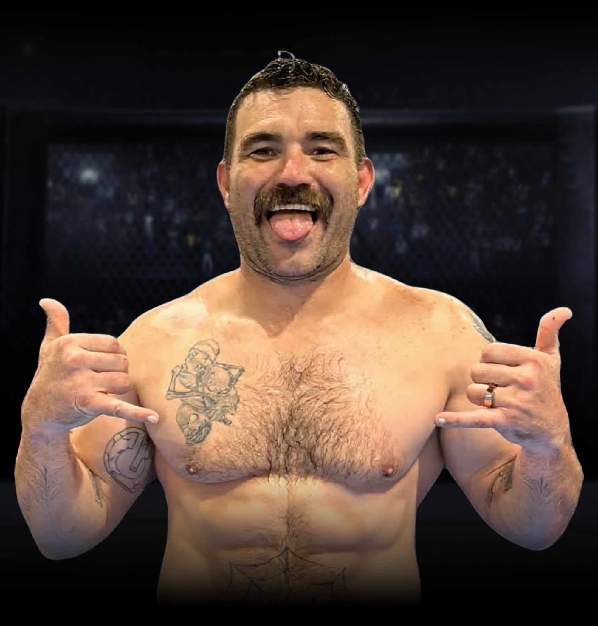 A shirtless man with a beard and short hair sticking his tongue out, smiling, with tattoos on his chest and arms, standing in front of a black background, giving a thumbs-up with both hands.