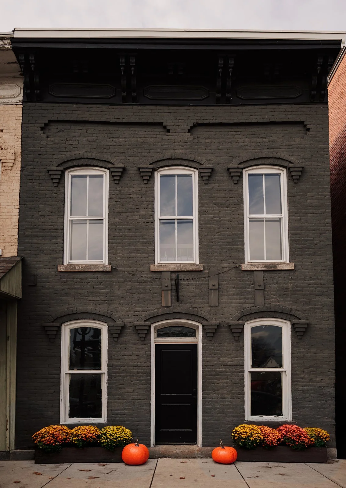 Person pouring wine into a glass on a table with a fire pit in the center of the table. In the background, two women are seated, and a third woman is standing. The setting appears to be a cozy indoor space with warm lighting and wooden decor.