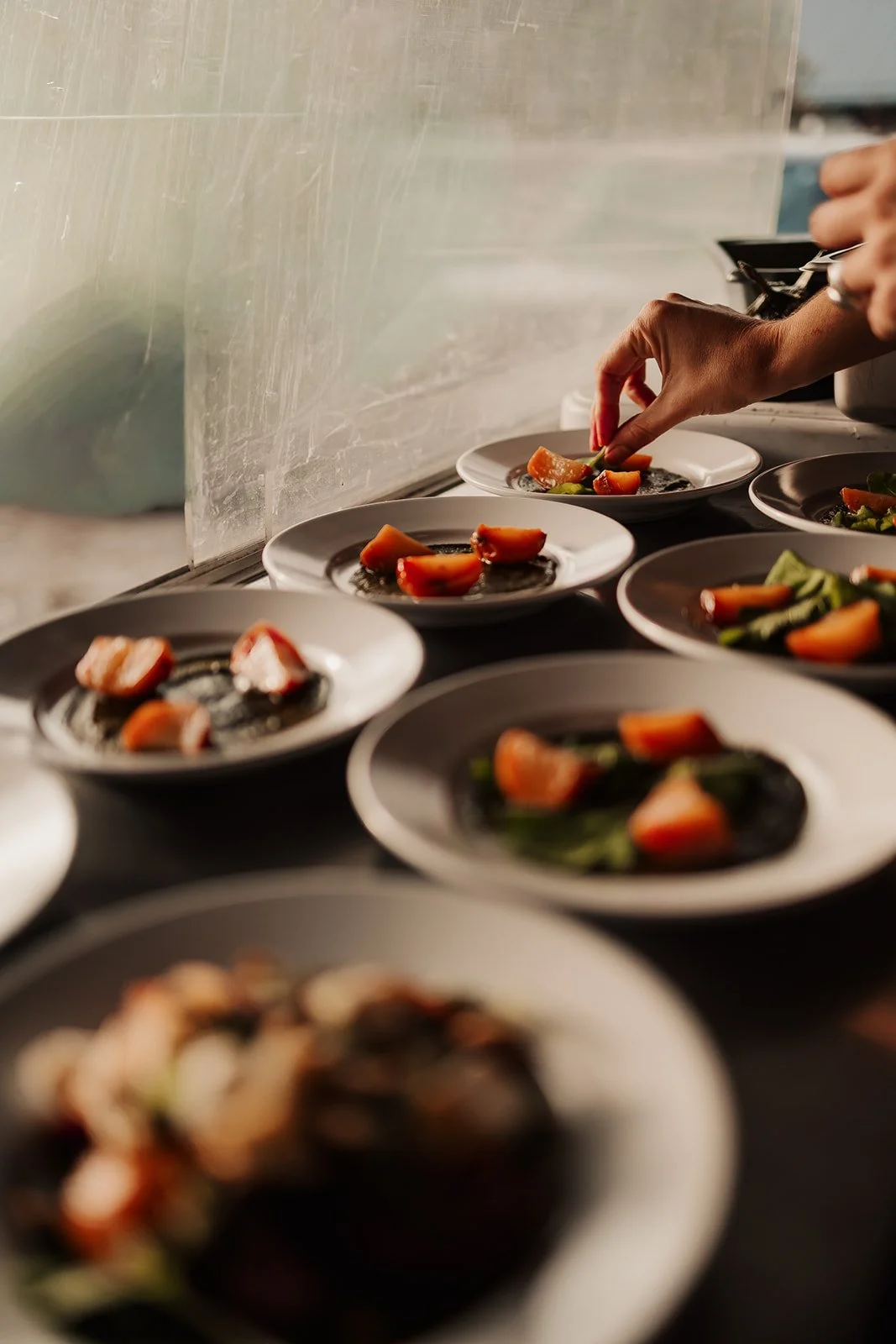 Chef plating small dishes with vegetables on white plates in a professional kitchen.