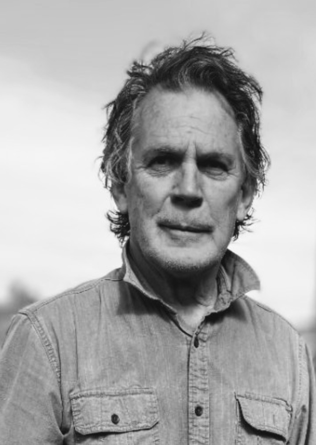 Black and white photo of a man with wavy hair, wearing a jacket and a collared shirt.