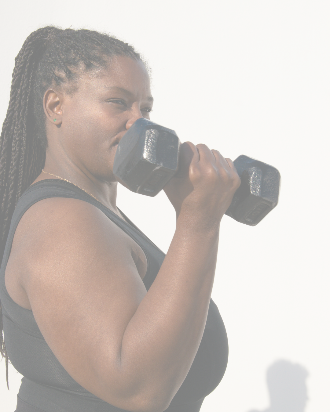 A woman with braids in a black tank top lifting dumbbells and smiling.