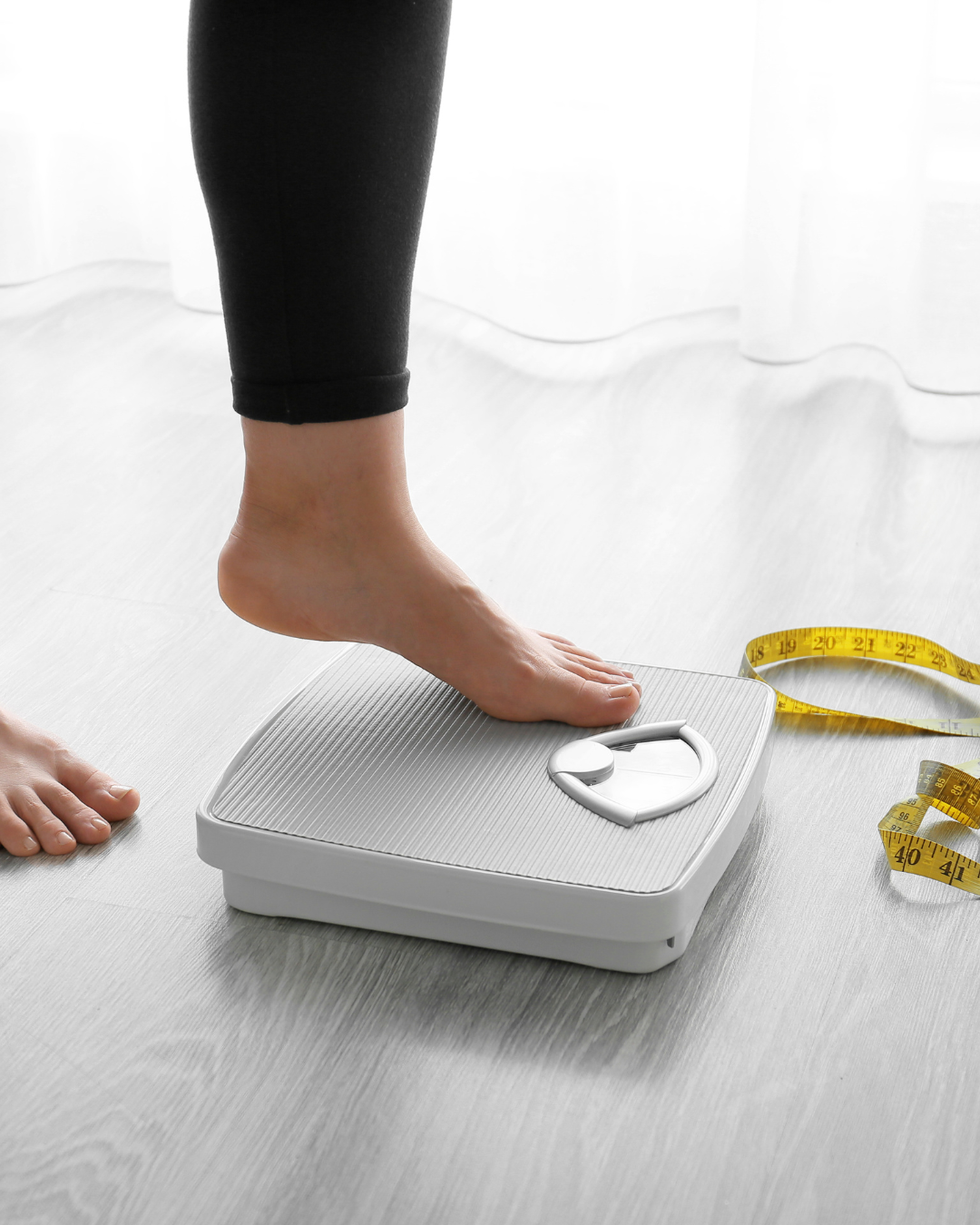 Person standing on a digital bathroom scale, measuring weight, with a yellow measuring tape nearby.