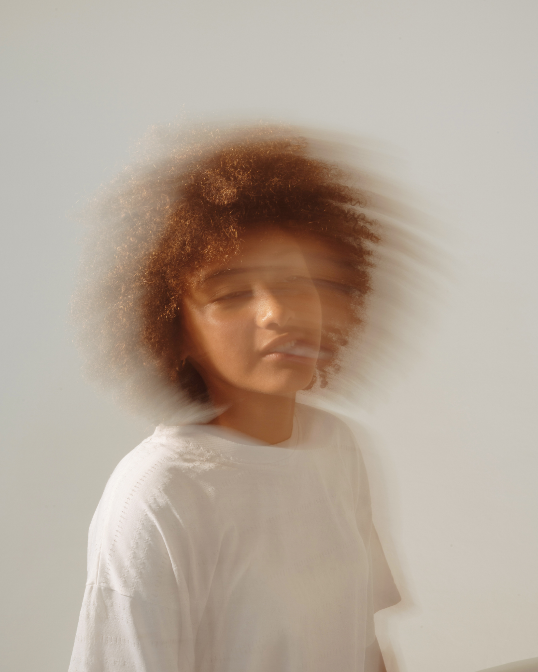 A woman with curly hair appears blurred, creating a motion effect, against a plain light background.