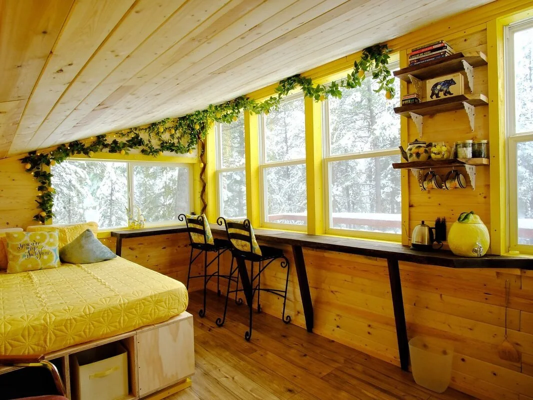 Interior of The Ranch Hand cabin showing a queen bed and views of the Montana forest through large windows.