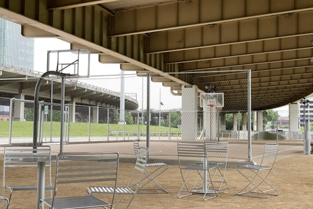 Empty outdoor basketball court with metal chairs and tables under an overpass.