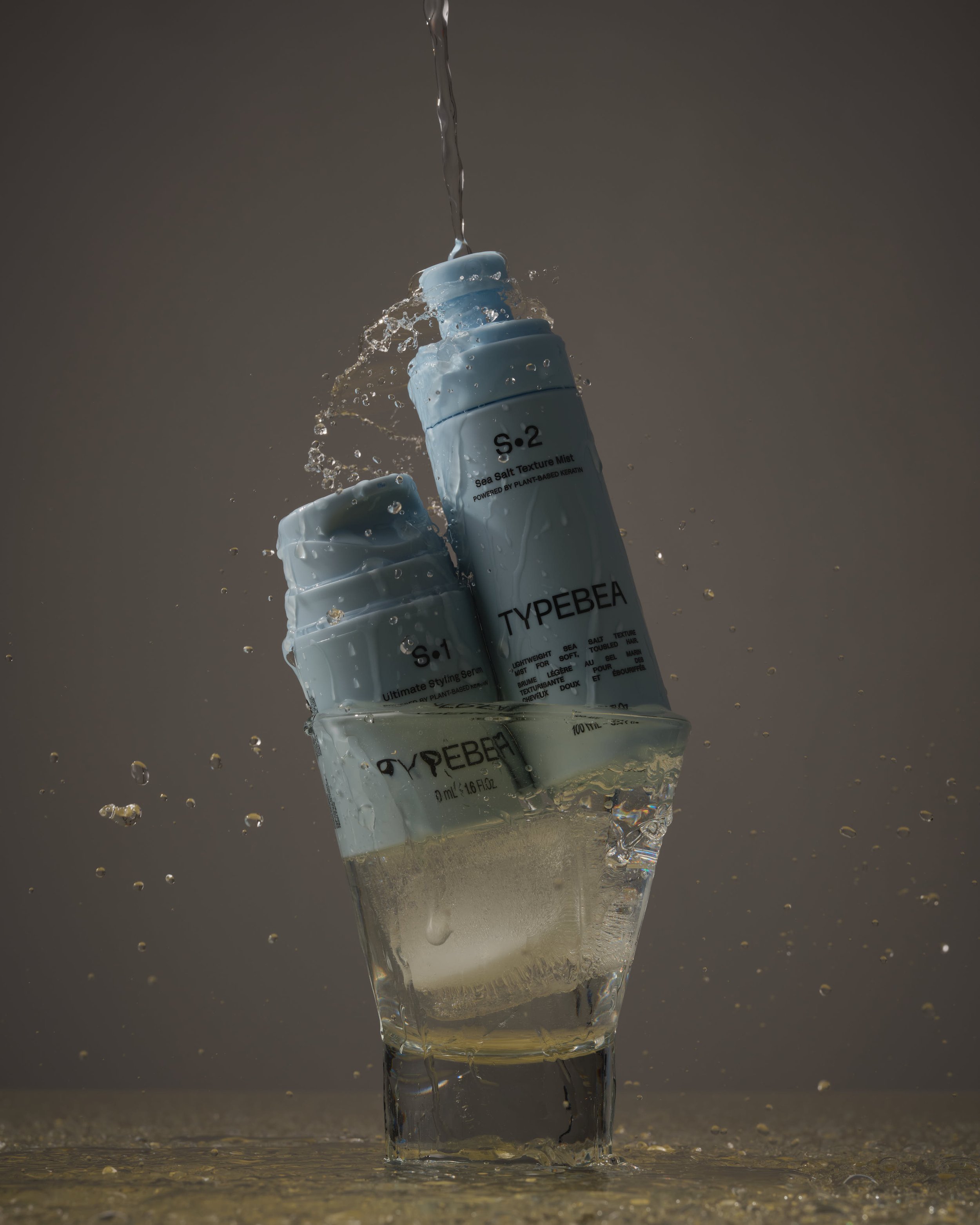 A light blue bottle of hair styling serum submerged in water with water splashing and droplets around it, on a dark background.