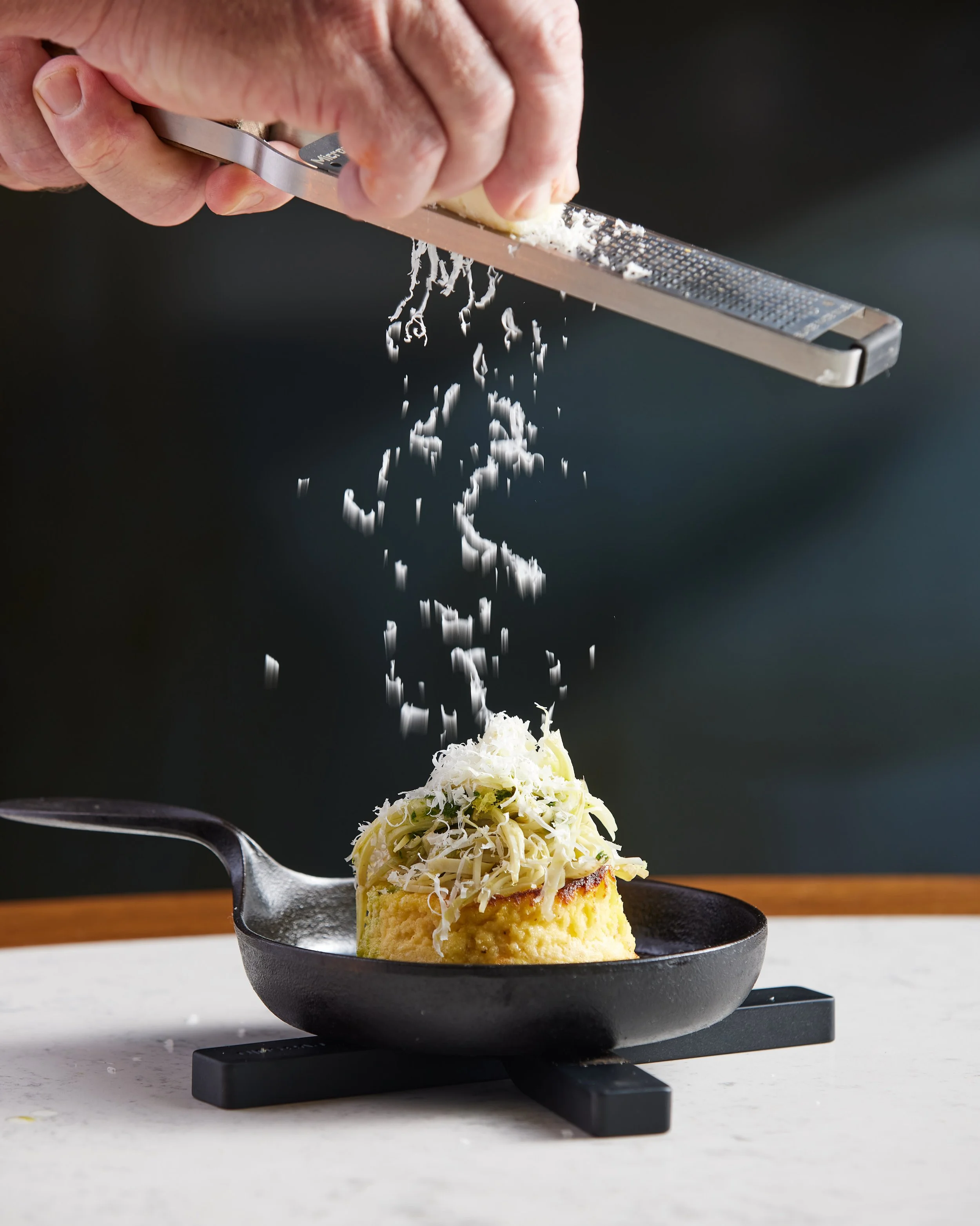 Person grating cheese over a baked dish in a black skillet.
