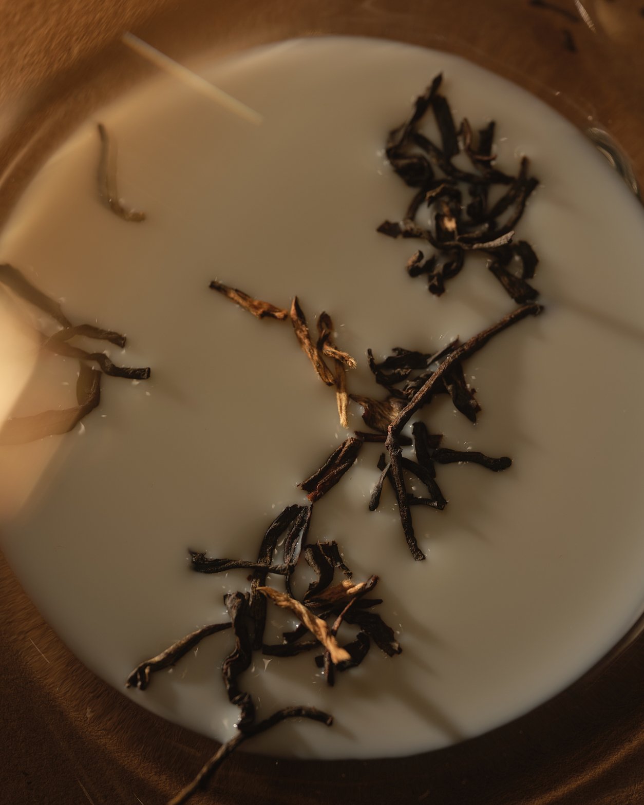 A close-up of a bowl filled with cream-colored liquid, garnished with dark, dried tea leaves or herbs.
