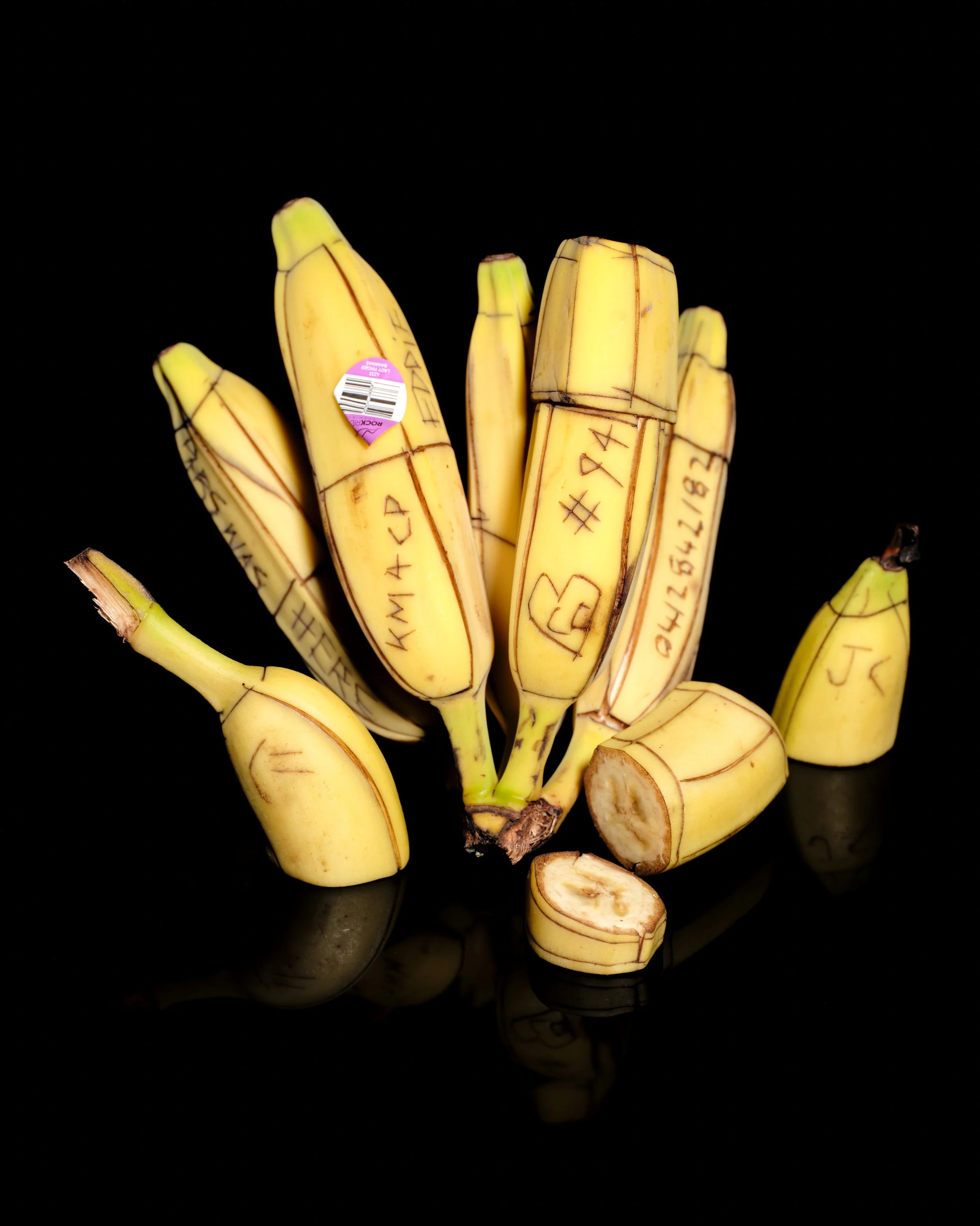 Cluster of small yellow bananas with black markings on a black reflective surface