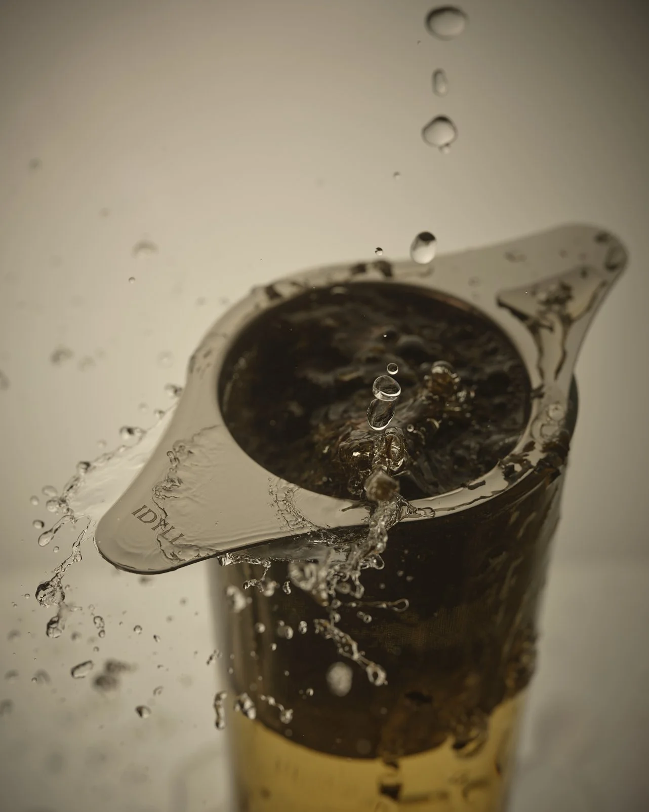 A close-up of a metal measuring cup filled with dark liquid, with water splashing out of it and droplets in mid-air.