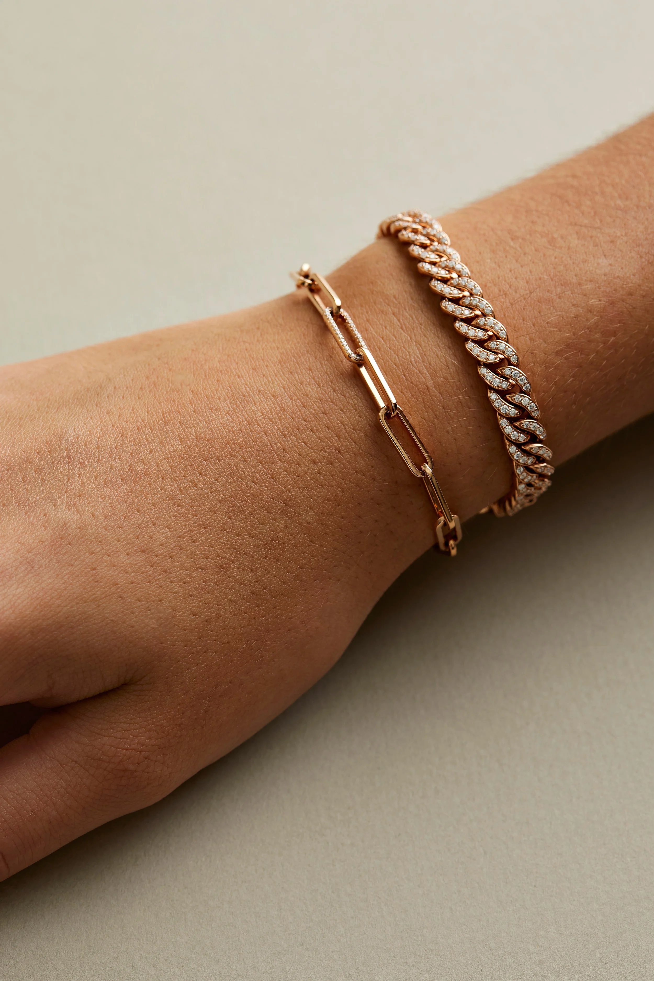 Close-up of a person wearing two gold bracelets on their wrist, one with a chain link design and the other with a diamond-studded, braided pattern.