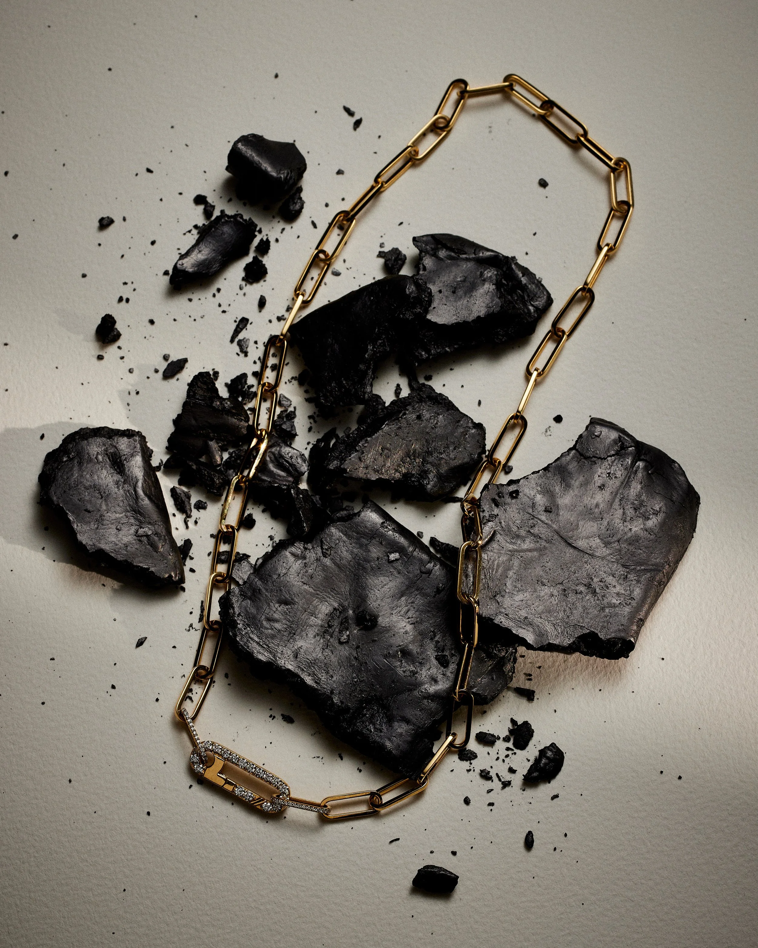 Broken black ceramic pieces and a gold chain necklace on a plain surface.