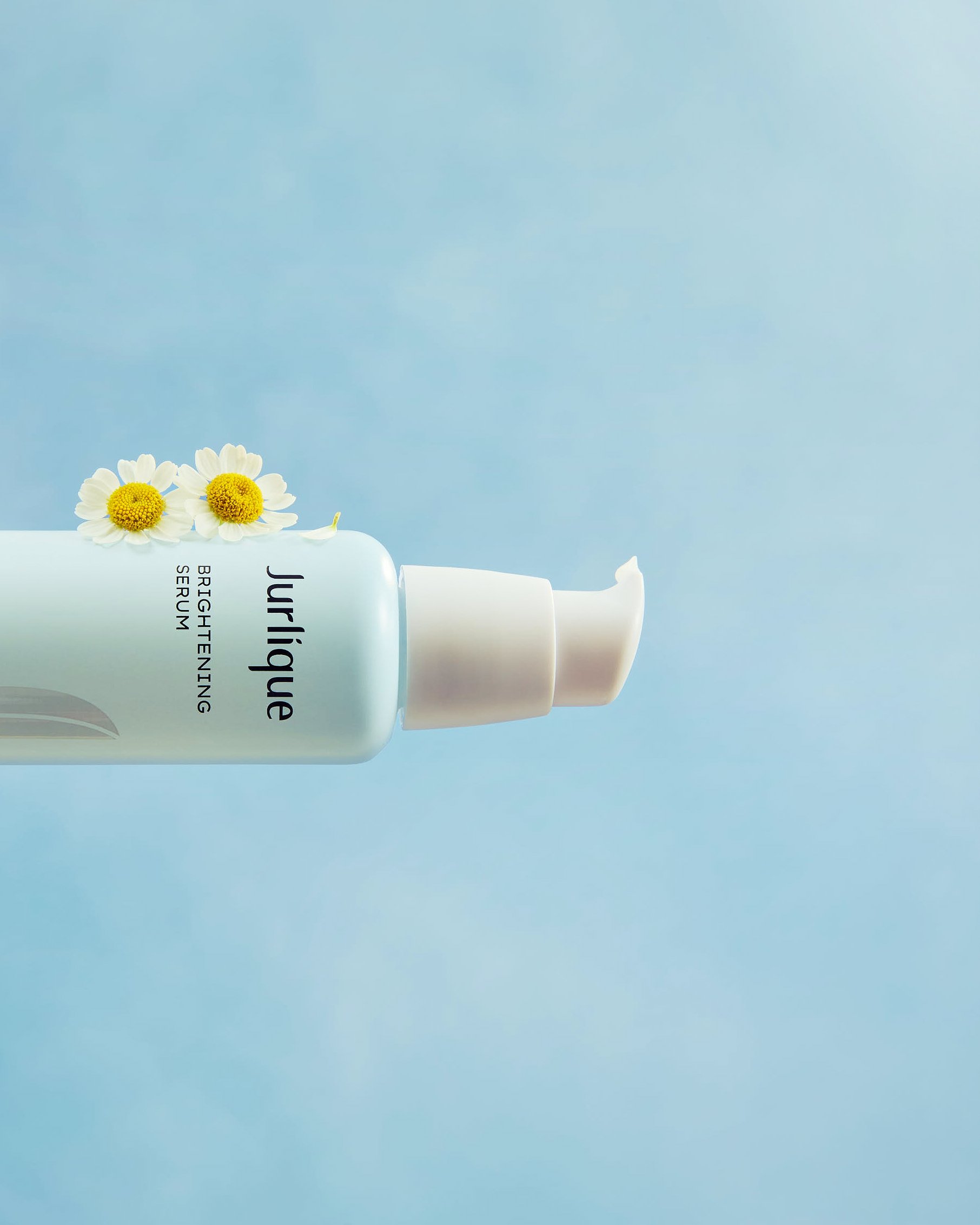 Part of a white skincare or haircare bottle with a pump dispenser, decorated with white daisies with yellow centers against a light blue background.