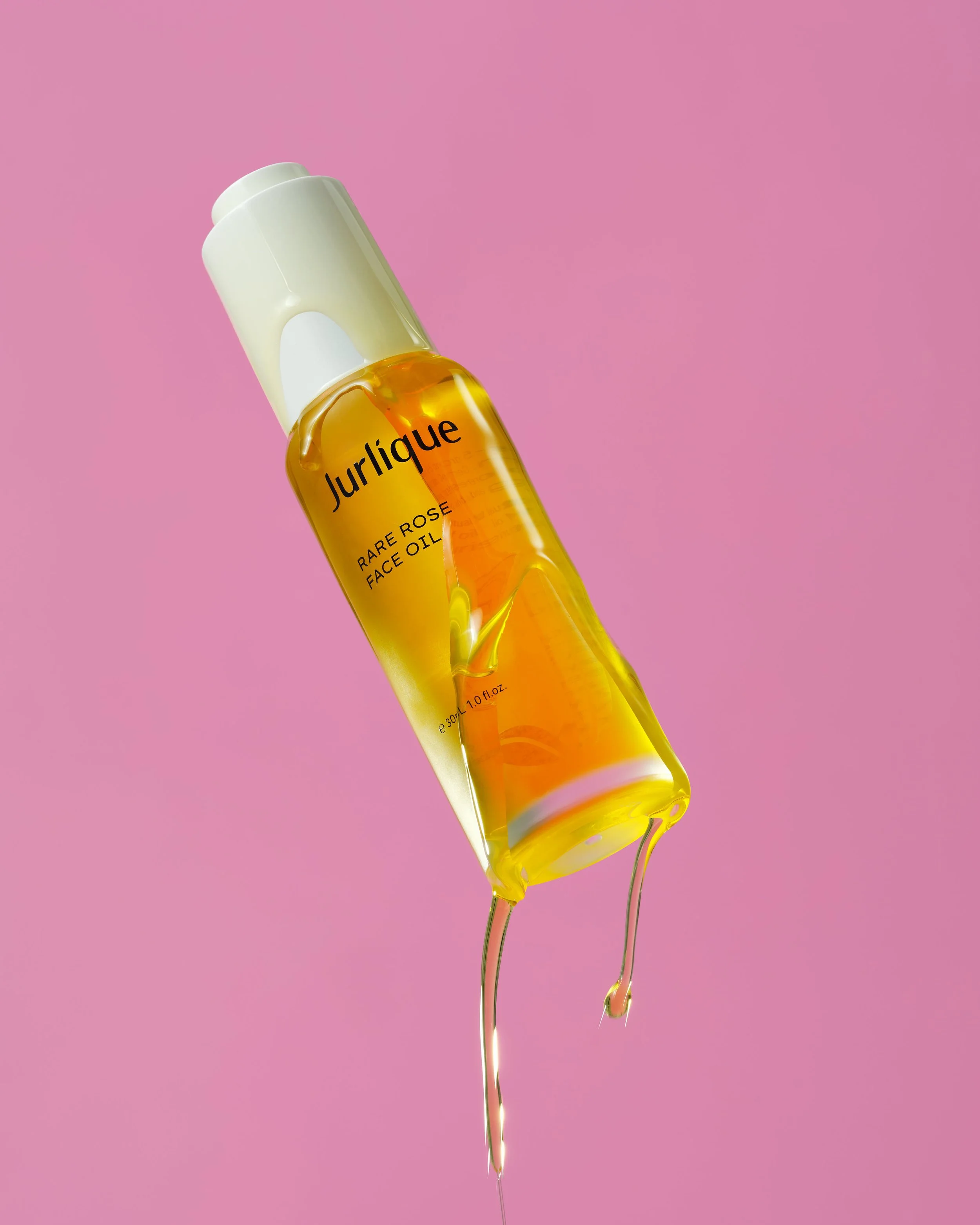 A bottle of Jurlique Rare Rose Face Oil with the oil spilling from the bottle onto a pink background.