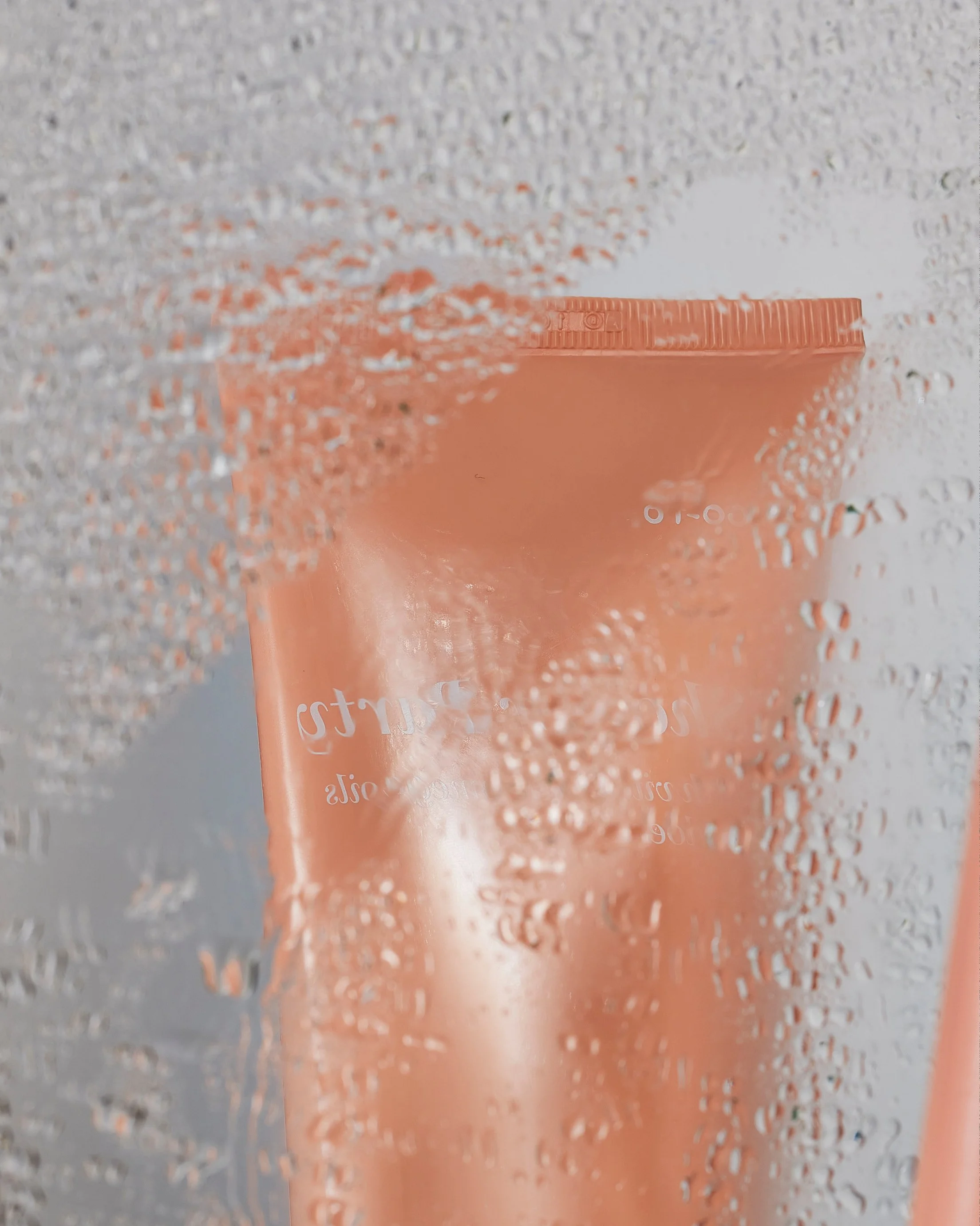 A pink bottle behind a foggy glass surface covered in condensation.