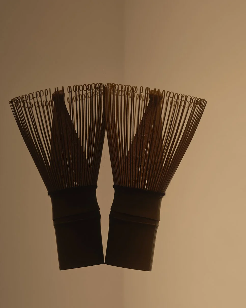 Two black bamboo whisks (chasen) used for making matcha tea, positioned vertically against a plain background.