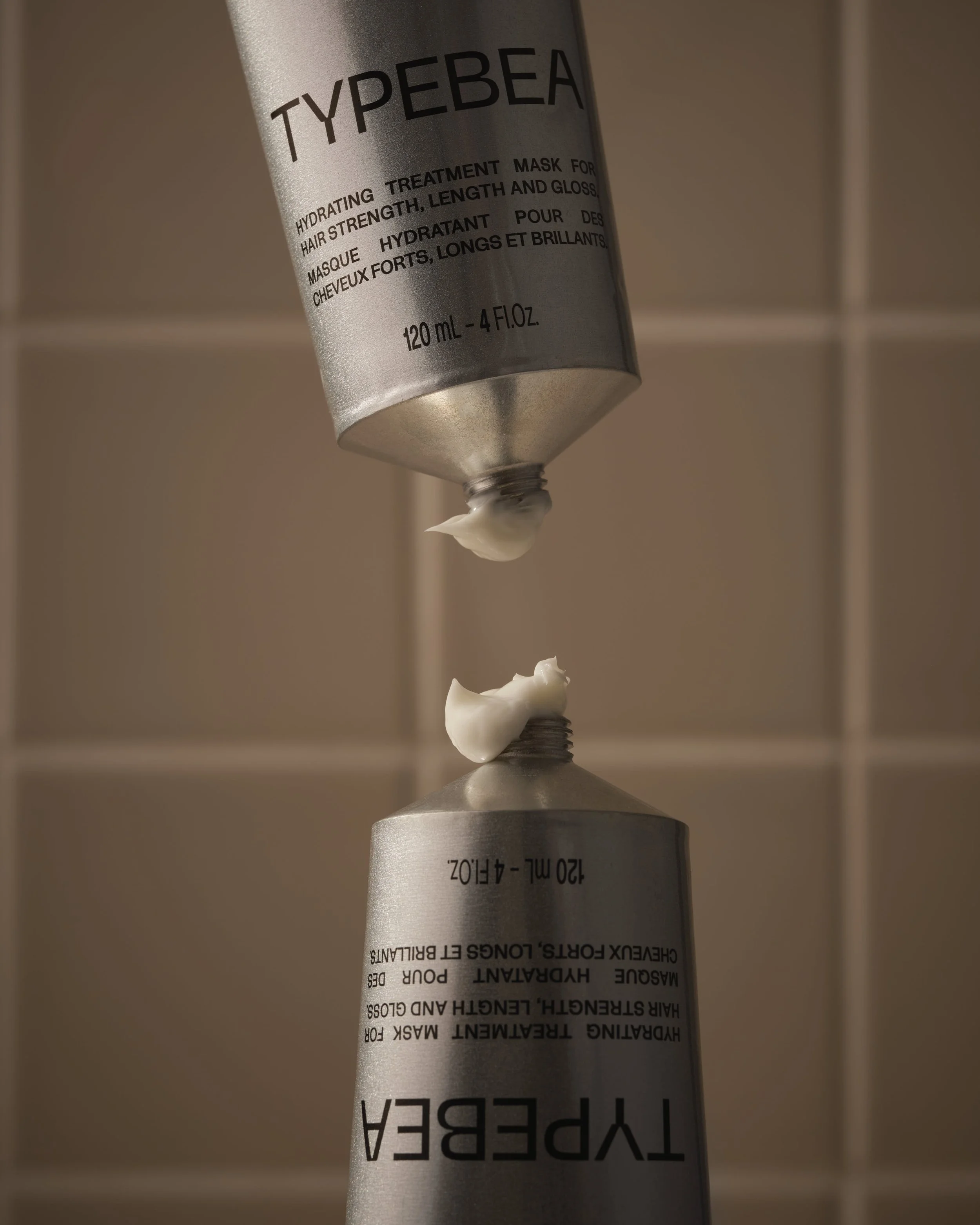 A tube of hydrating treatment mask for hair, with a dollop of cream falling from its nozzle.