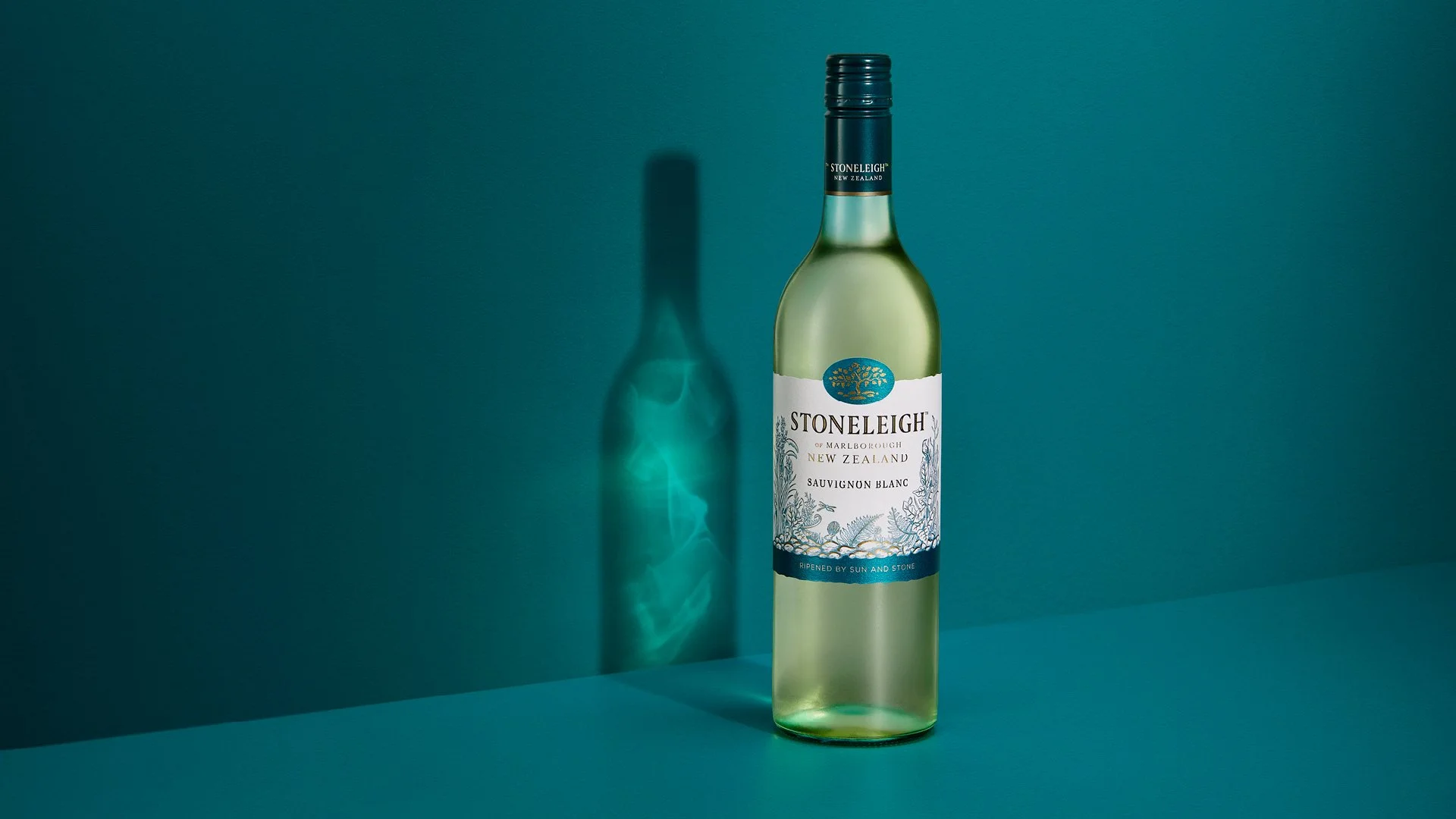 A bottle of Stoneleigh Sauvignon Blanc wine from New Zealand on a teal background, casting a shadow with a pattern of light reflection on the wall.