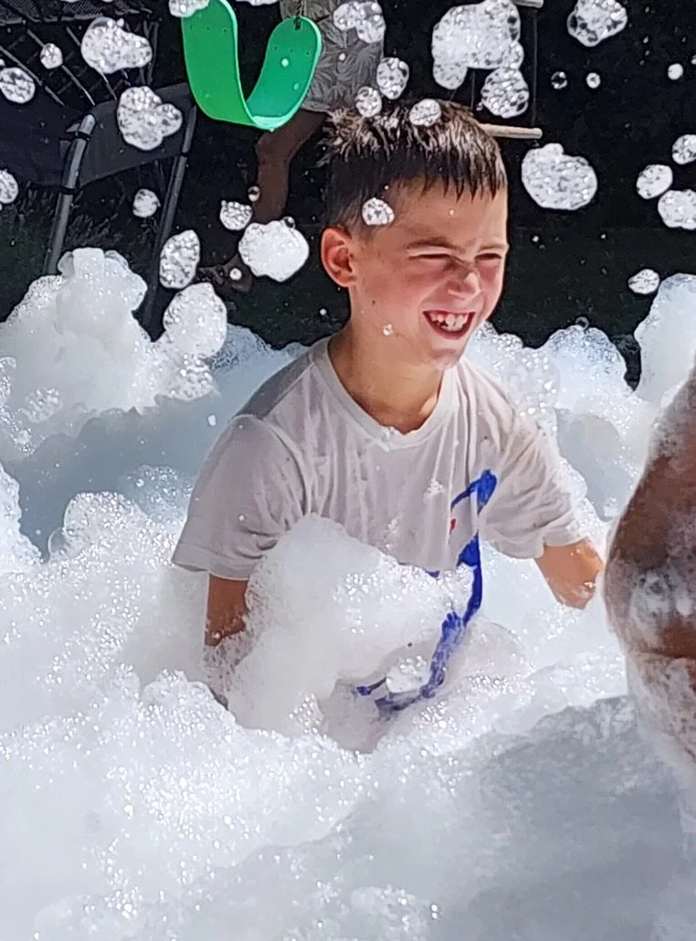 A young boy playing in a bubble bath, smiling and enjoying himself.