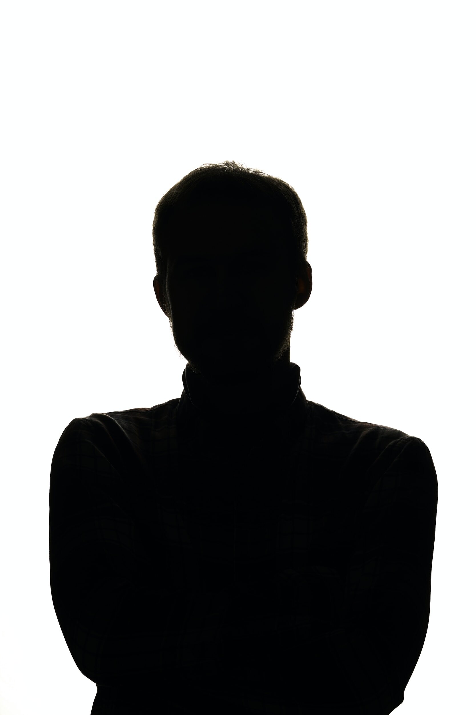 Silhouette of a person with arms crossed, facing away from the camera against a bright white background.