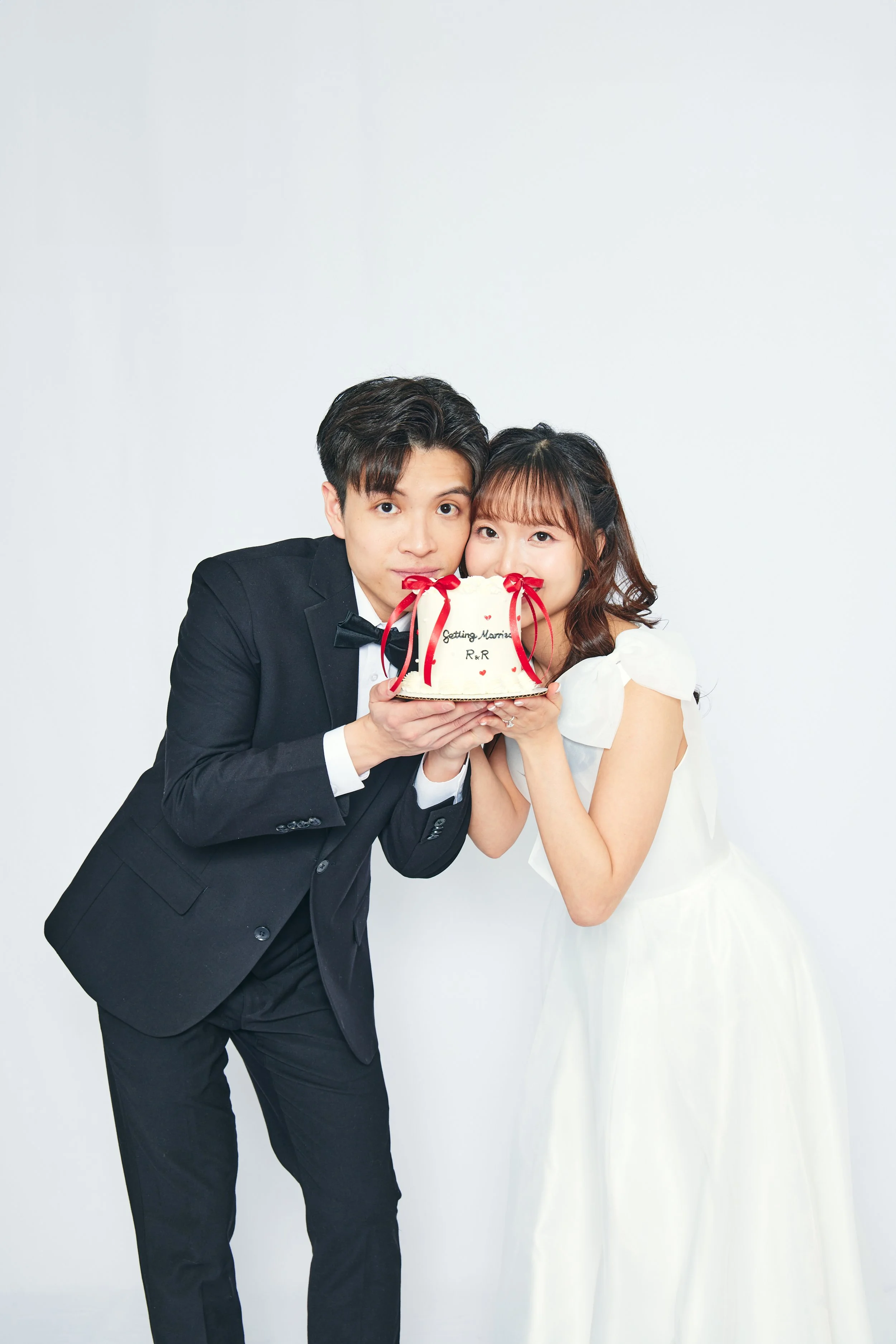 A couple dressed in wedding attire holding a cake with red ribbons, celebrating their marriage.