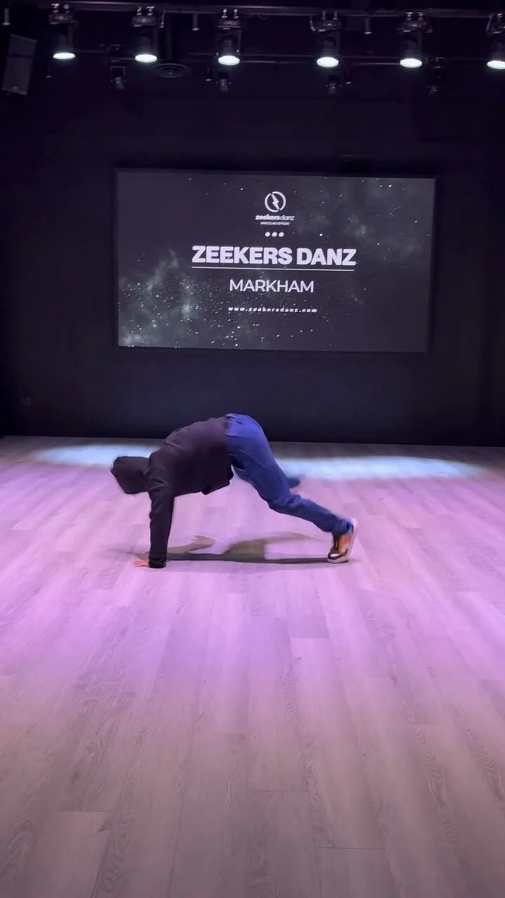 Reel still: a dancer low on the studio floor in front of a screen that reads Zeekers Danz Markham.