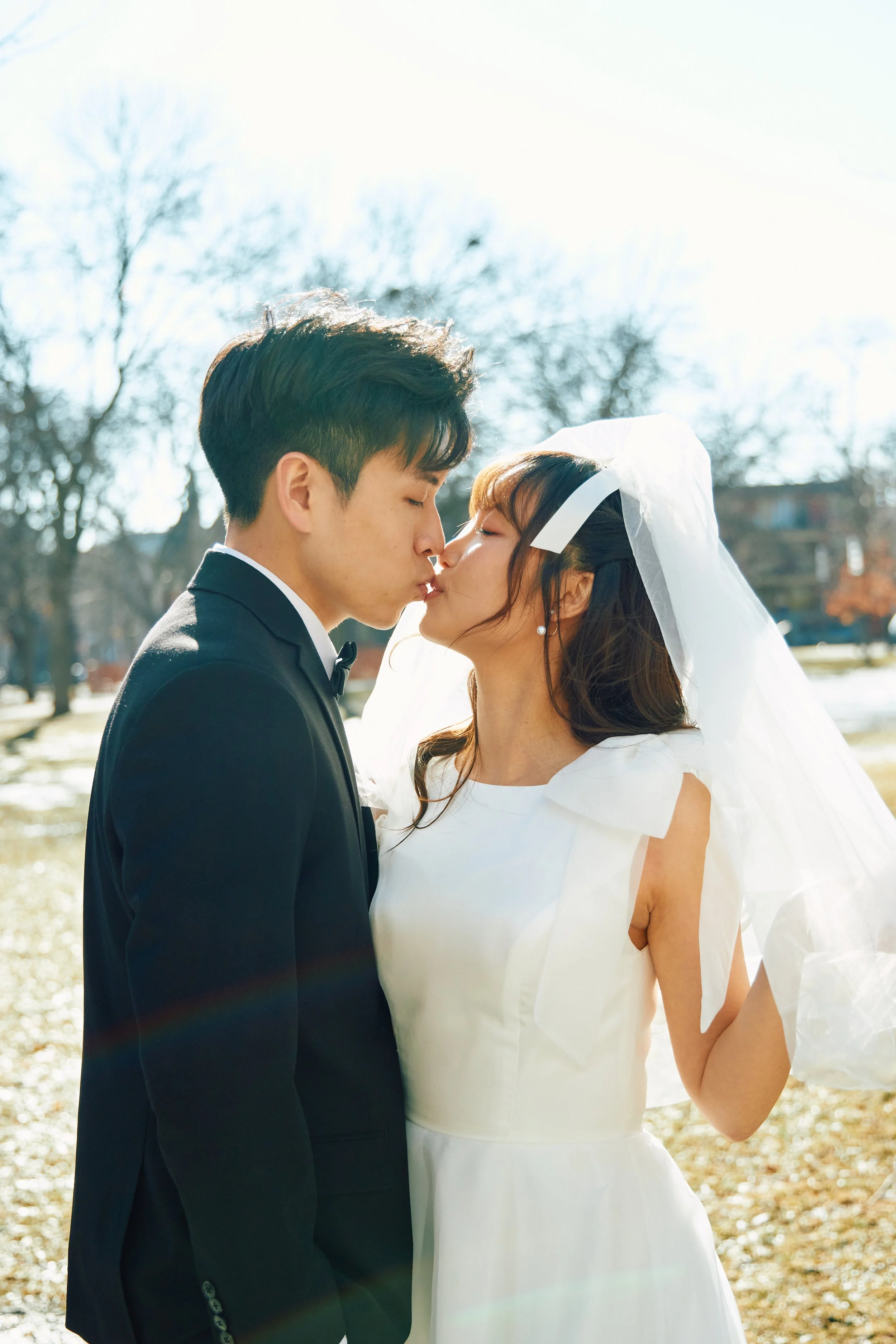 A bride and groom sharing a kiss outdoors on a sunny day.