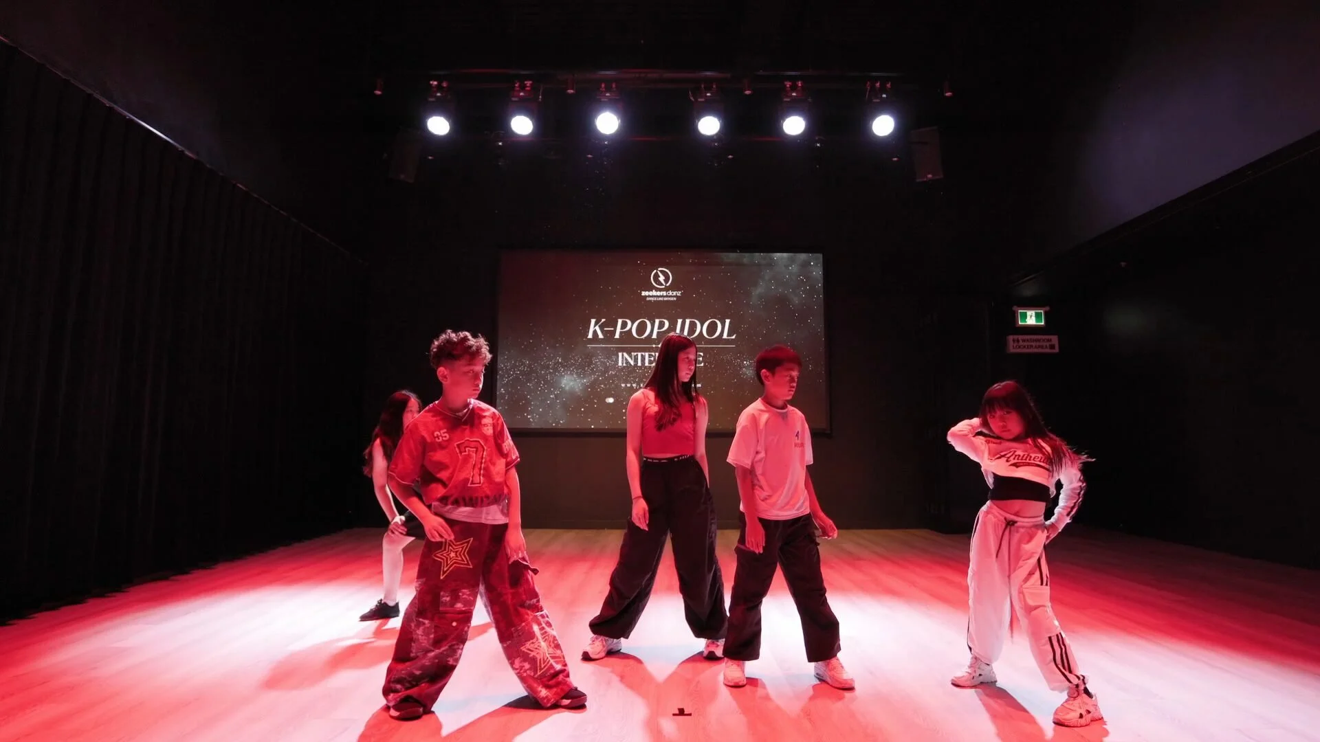 A camp team on the studio stage under red and blue lights, in front of a screen for the camp.