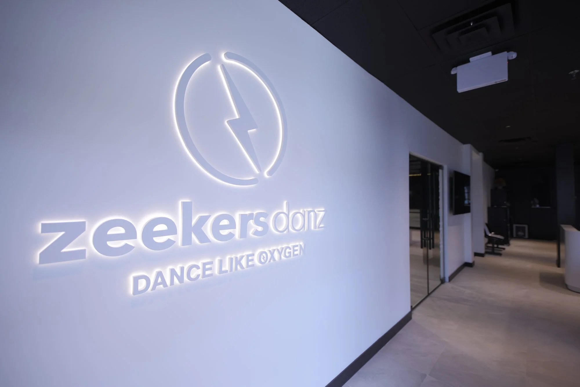 The lit ZeekersDanz logo on a white wall, with the line Dance Like Oxygen.