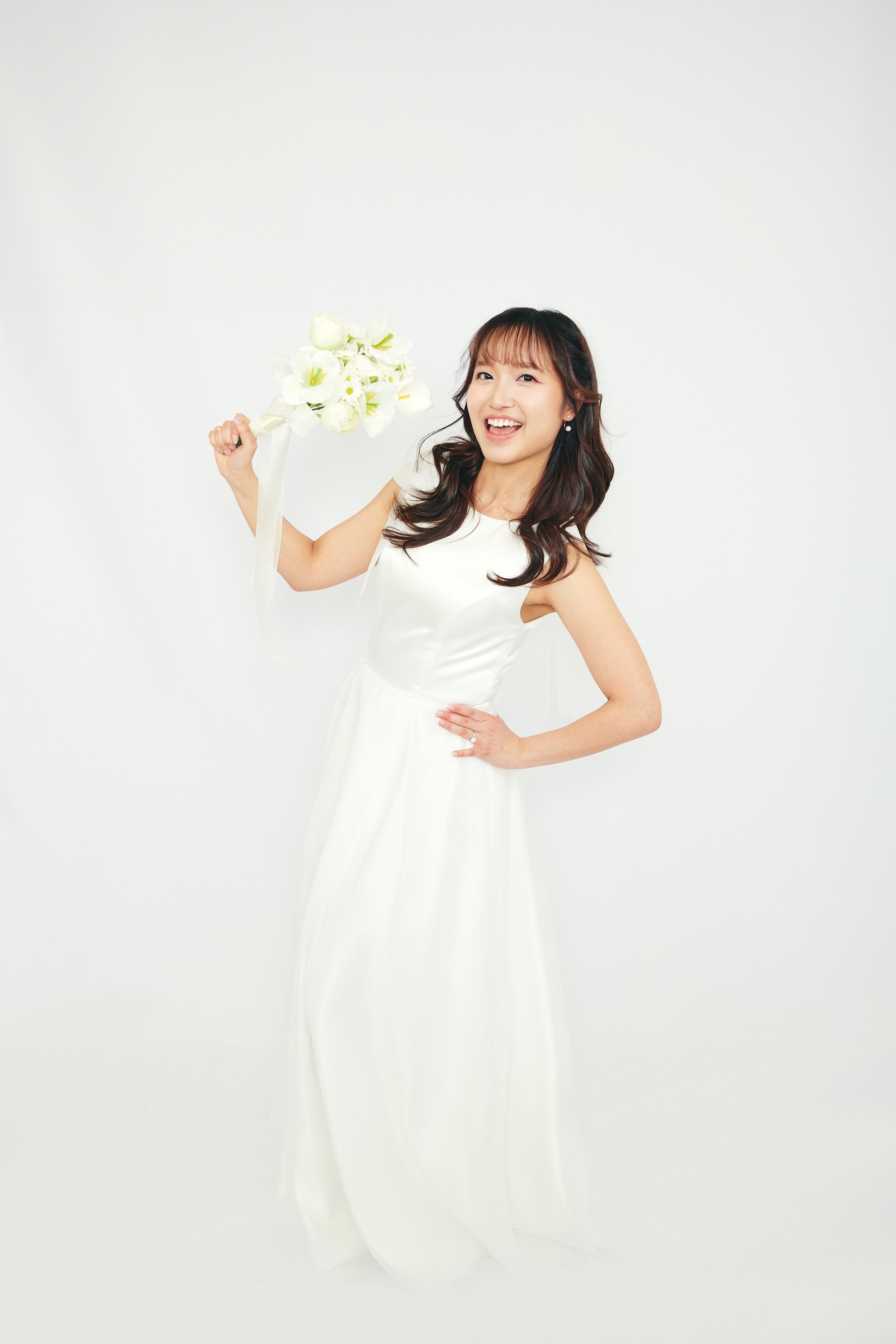 Young woman in wedding dress holding a bouquet of white flowers and smiling.