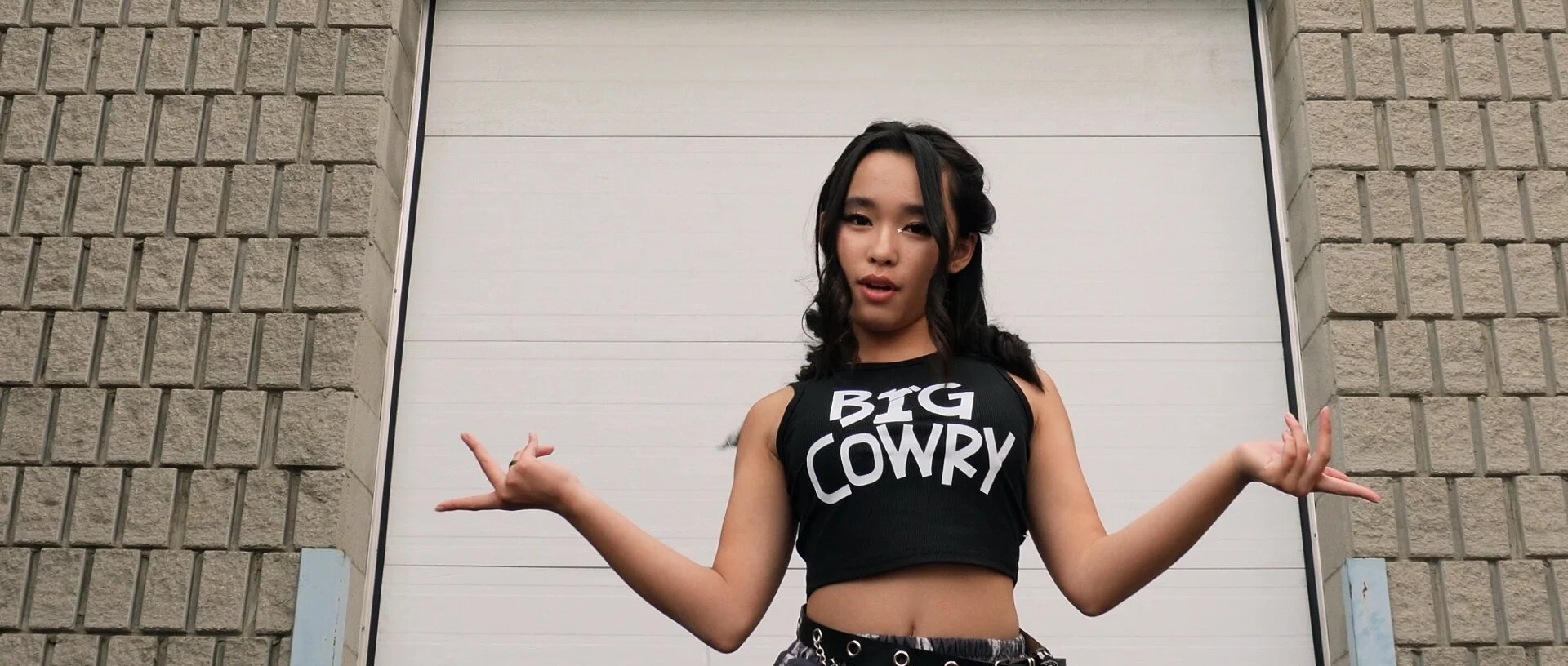 A dancer in a Big Cowry crop top in front of a white garage door, arms out.