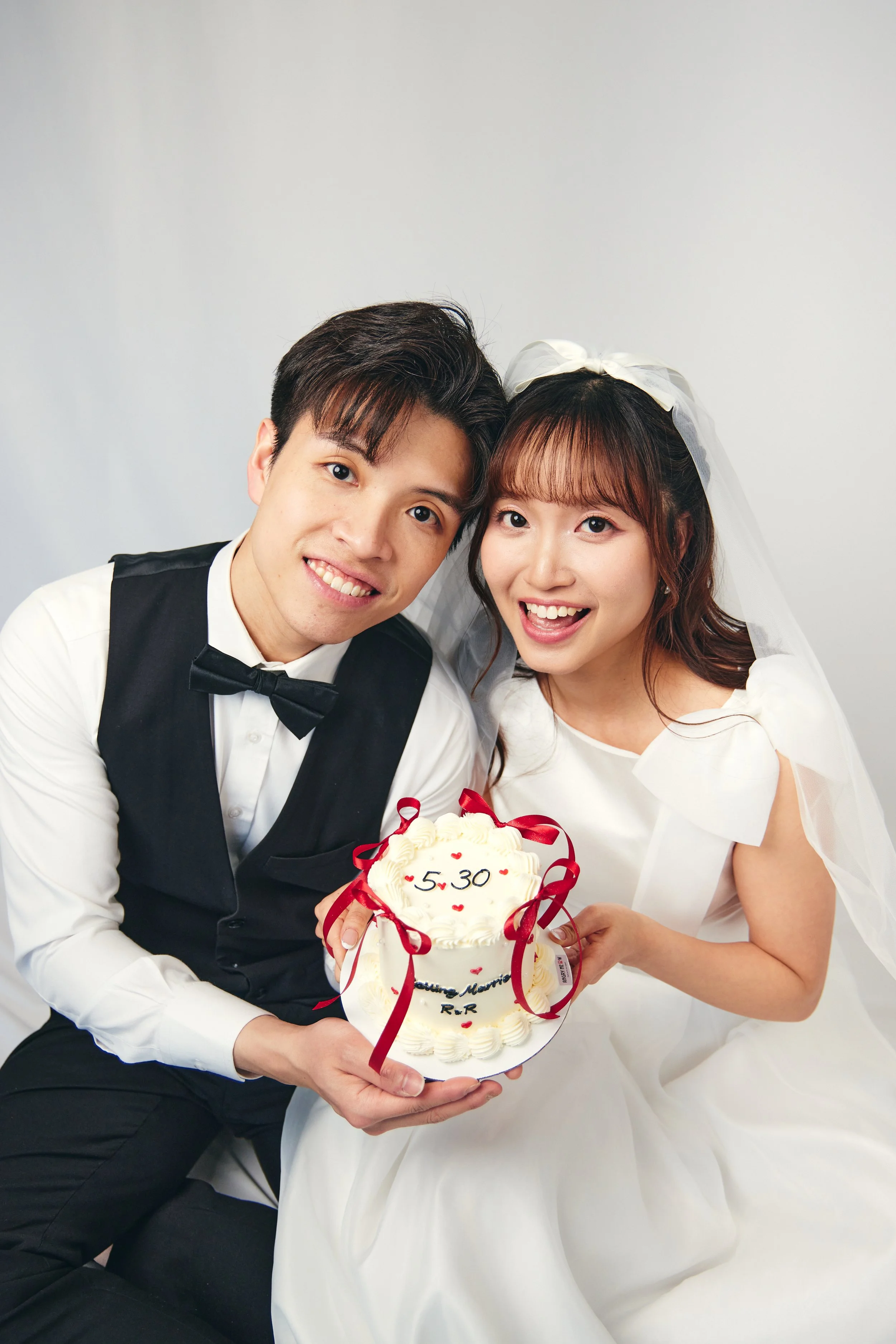 A happy bride and groom holding a wedding cake with the date 5.30 written on it, smiling at the camera.
