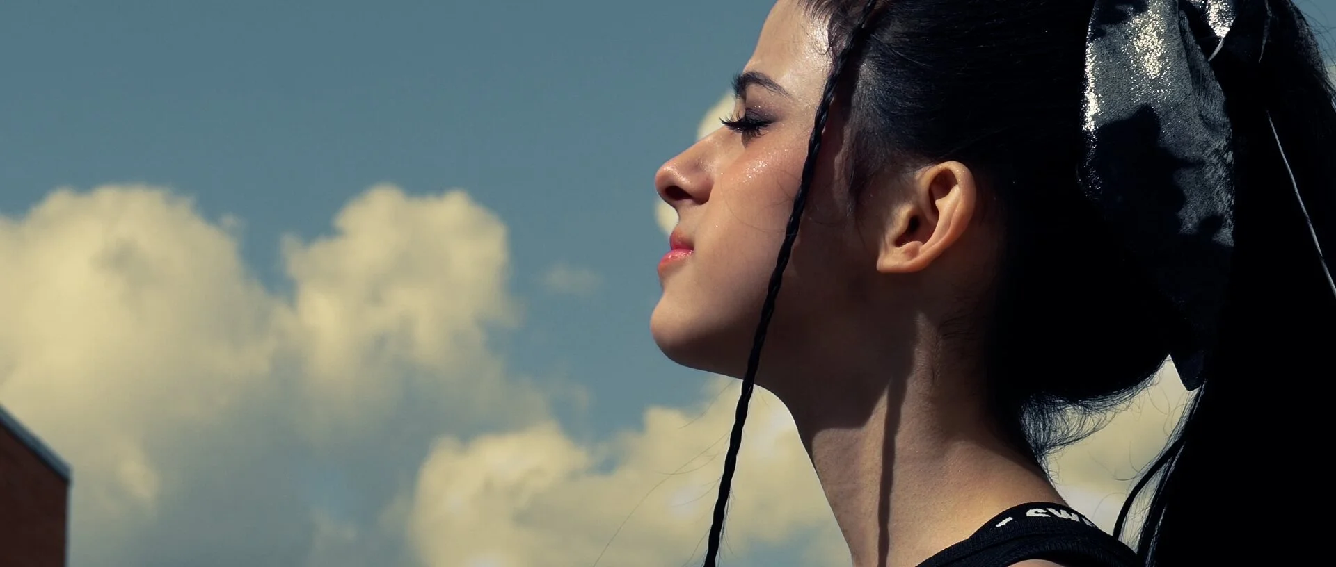 A dancer in profile against a cloudy sky, braids and a black bow in her hair.