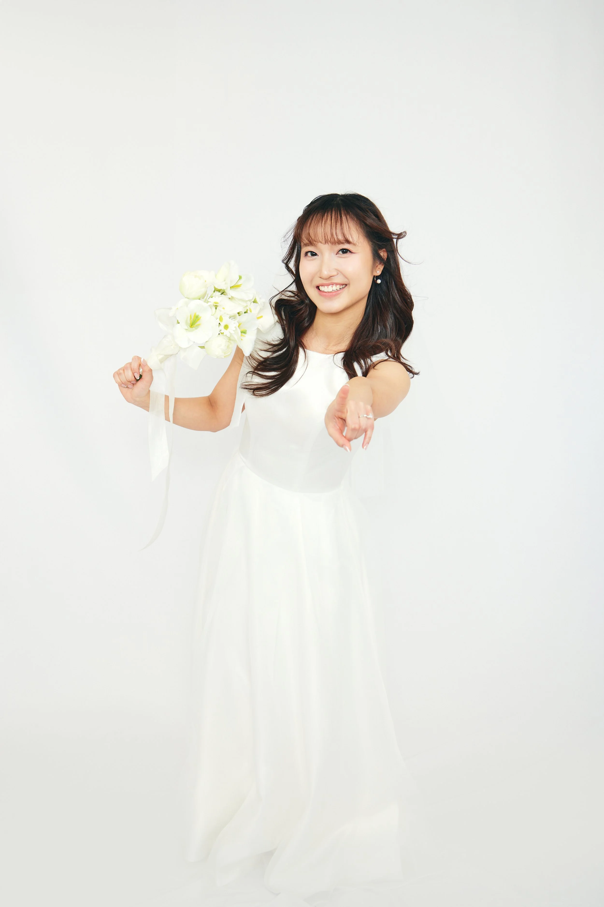 Woman in white dress holding a bouquet of white flowers and pointing forward.
