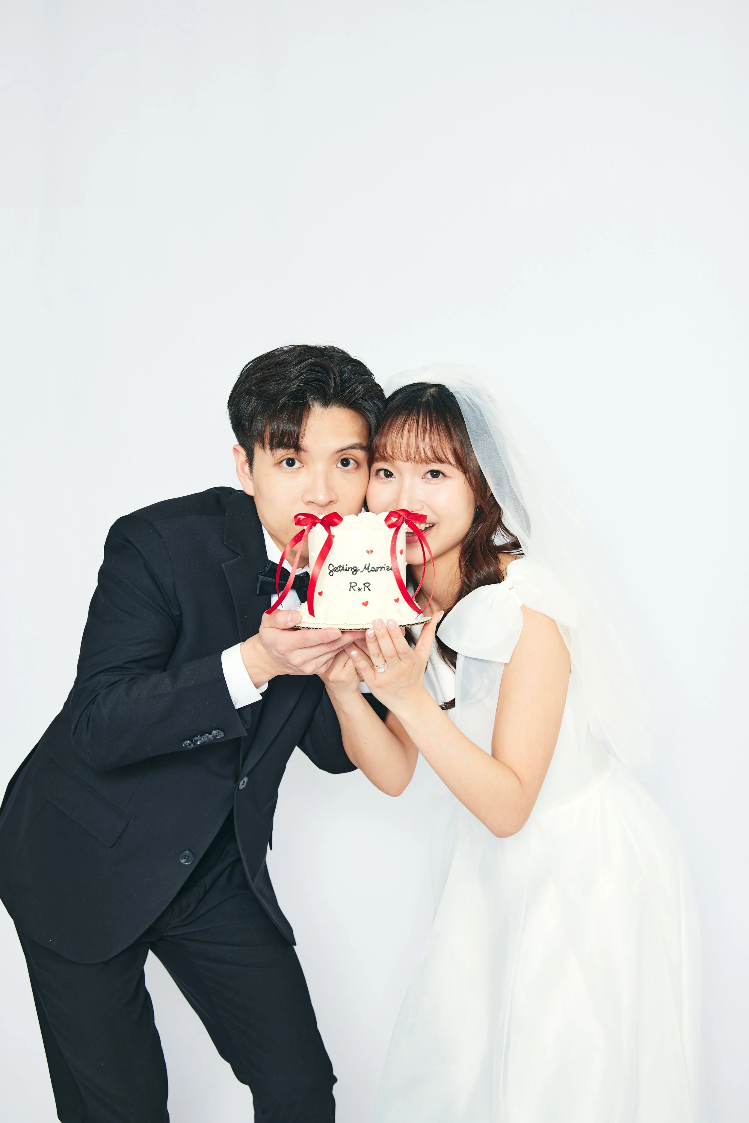 A newlywed couple in wedding attire holding a wedding cake and smiling.