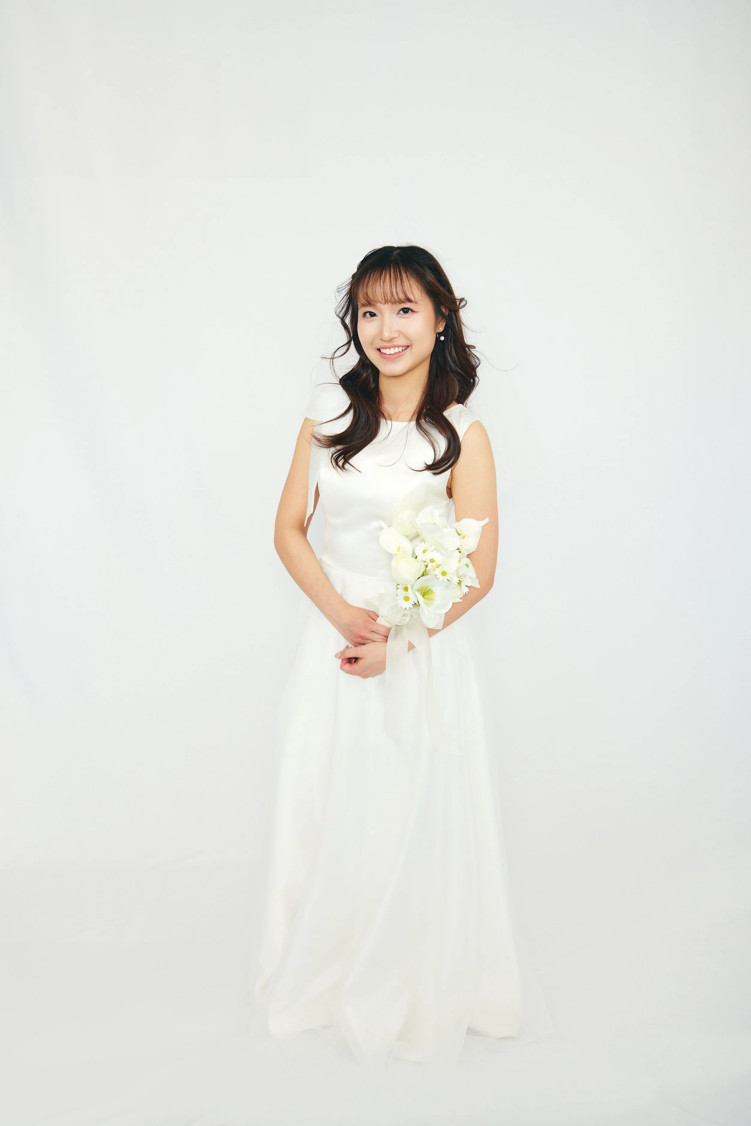 Young woman in a white dress holding a bouquet of white flowers, standing against a plain white background.