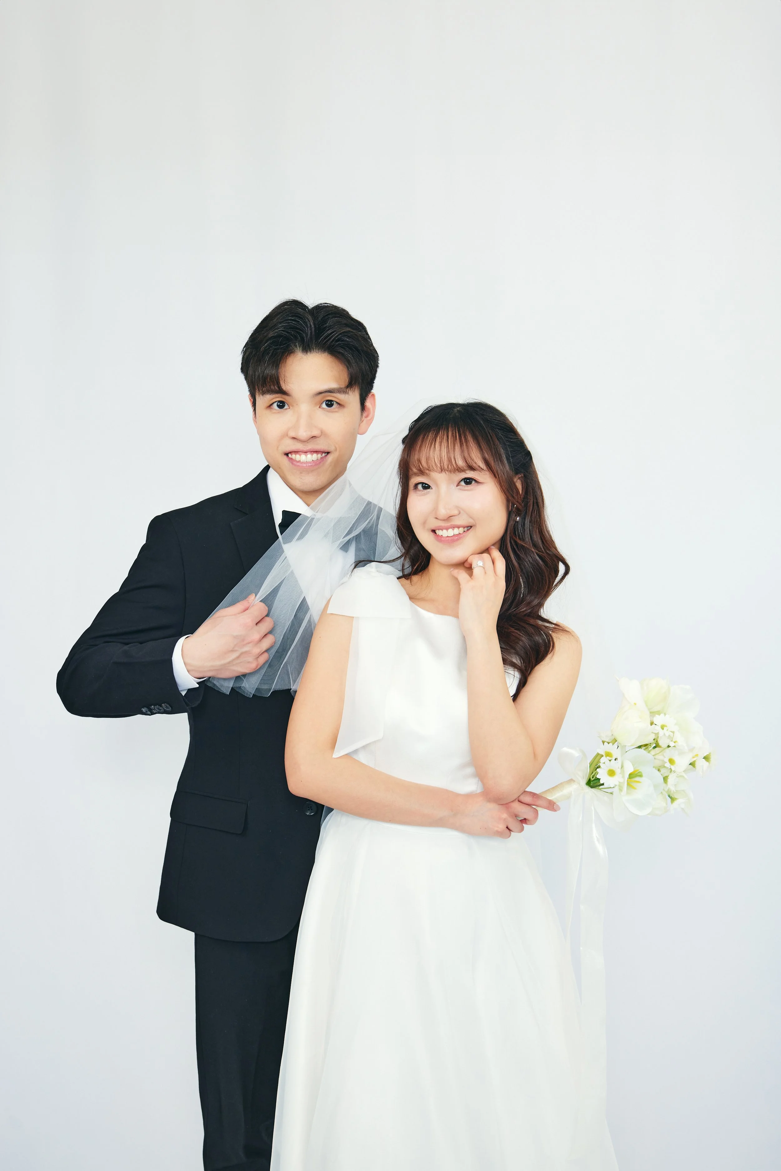 A young couple in wedding attire posing for a photo against a plain white background.
