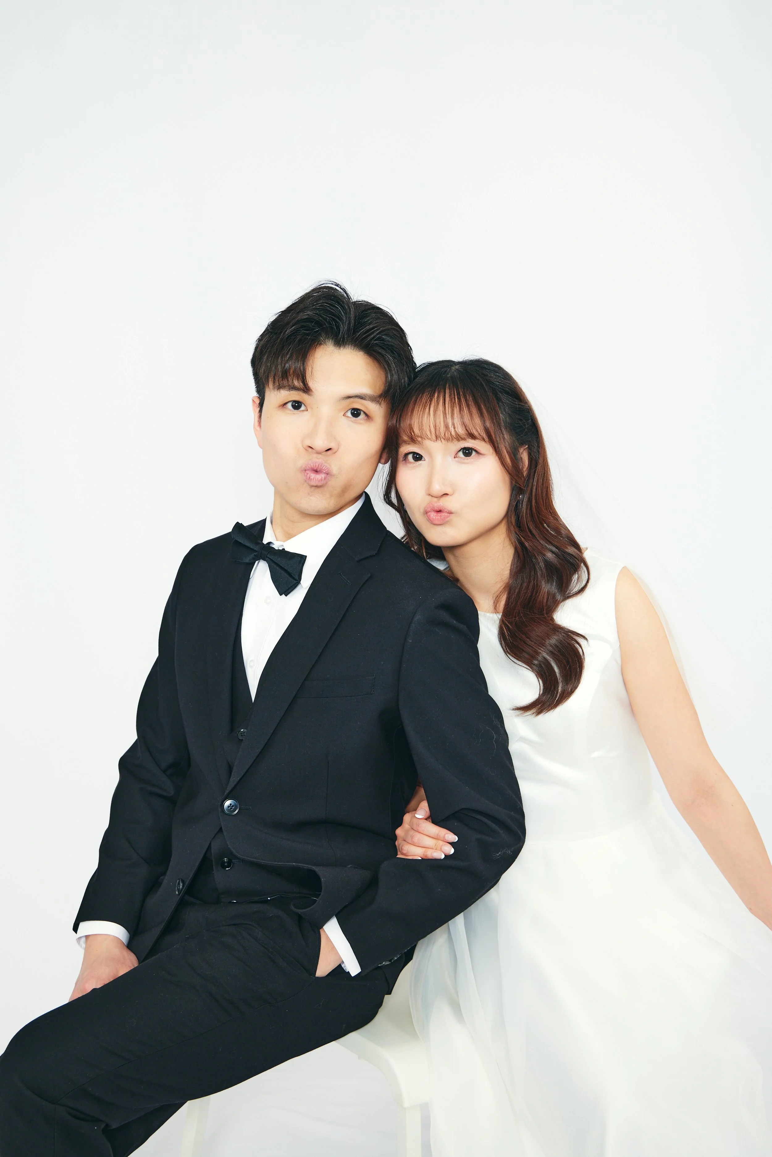 A well-dressed man and woman making kissy faces at the camera against a plain white background.