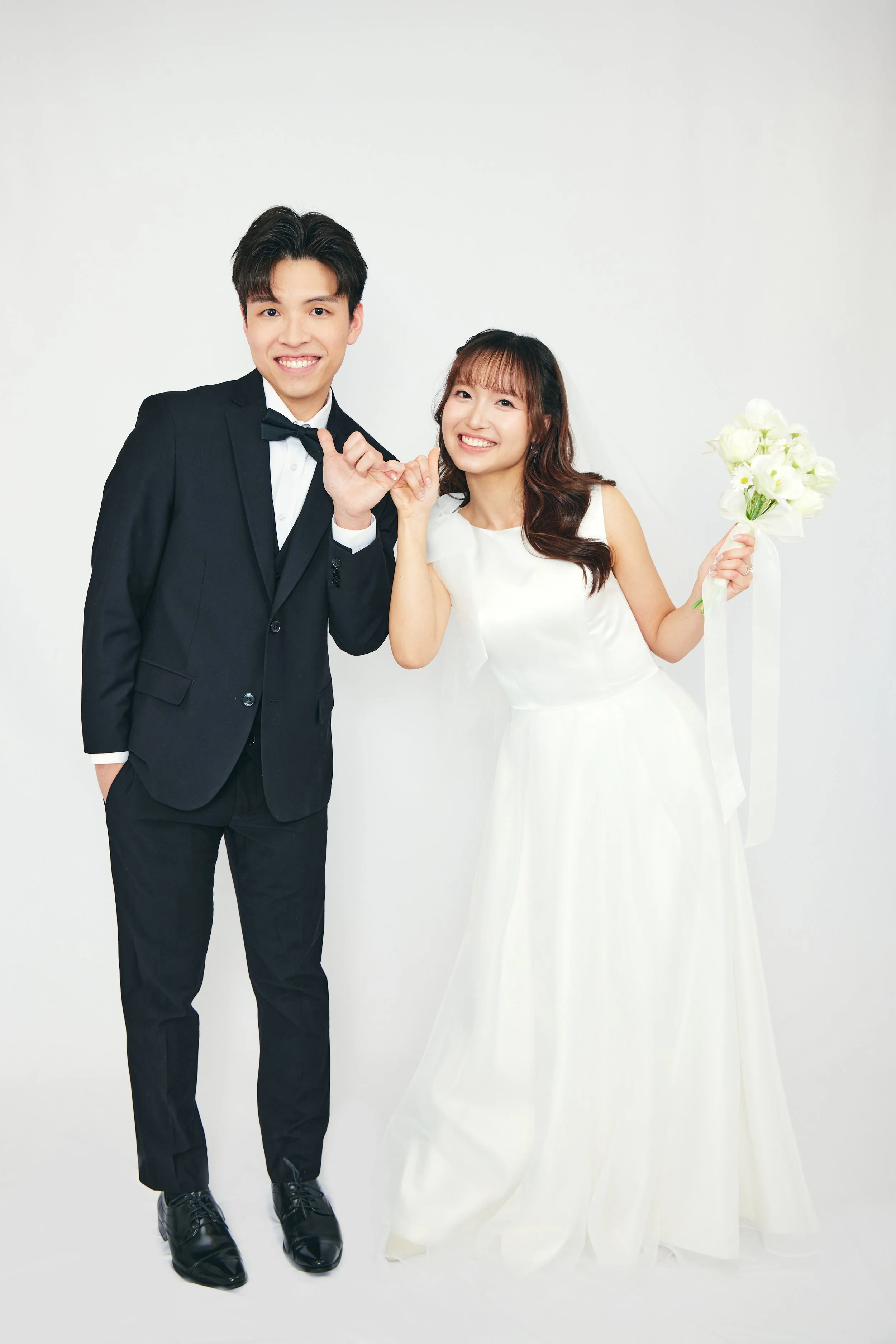 A happy bride and groom holding hands, smiling in wedding attire against a white background.