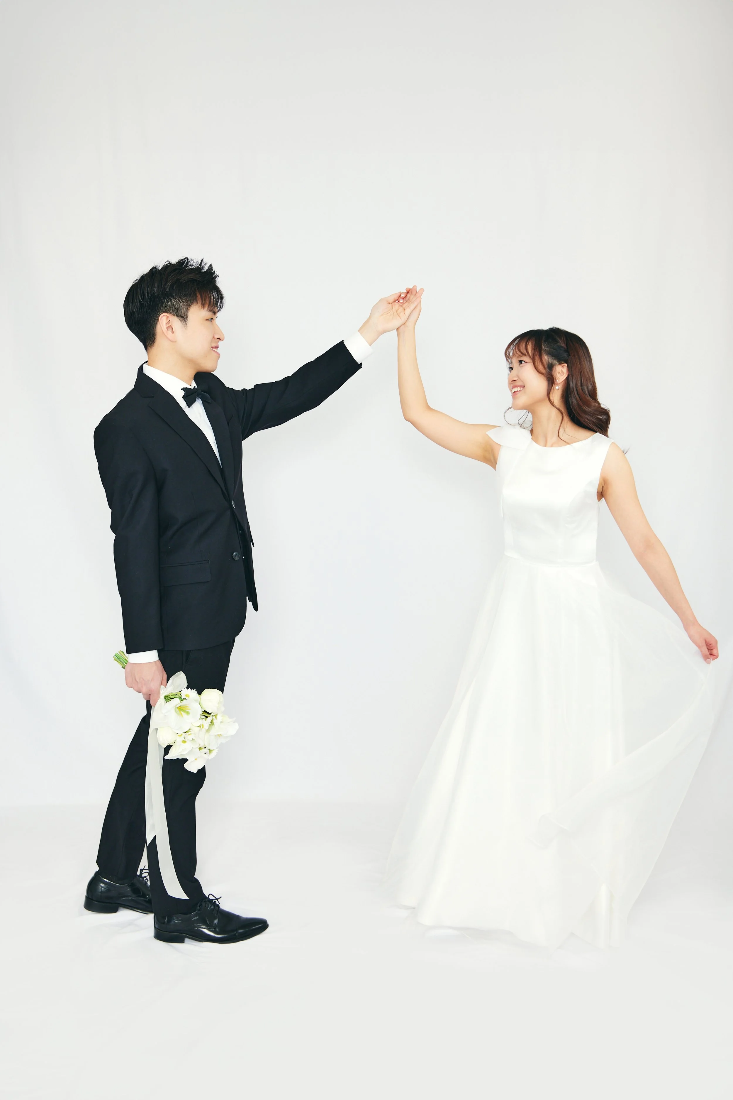 A bride and groom dancing together, with the groom holding a bouquet and the bride raising her hand, both smiling.