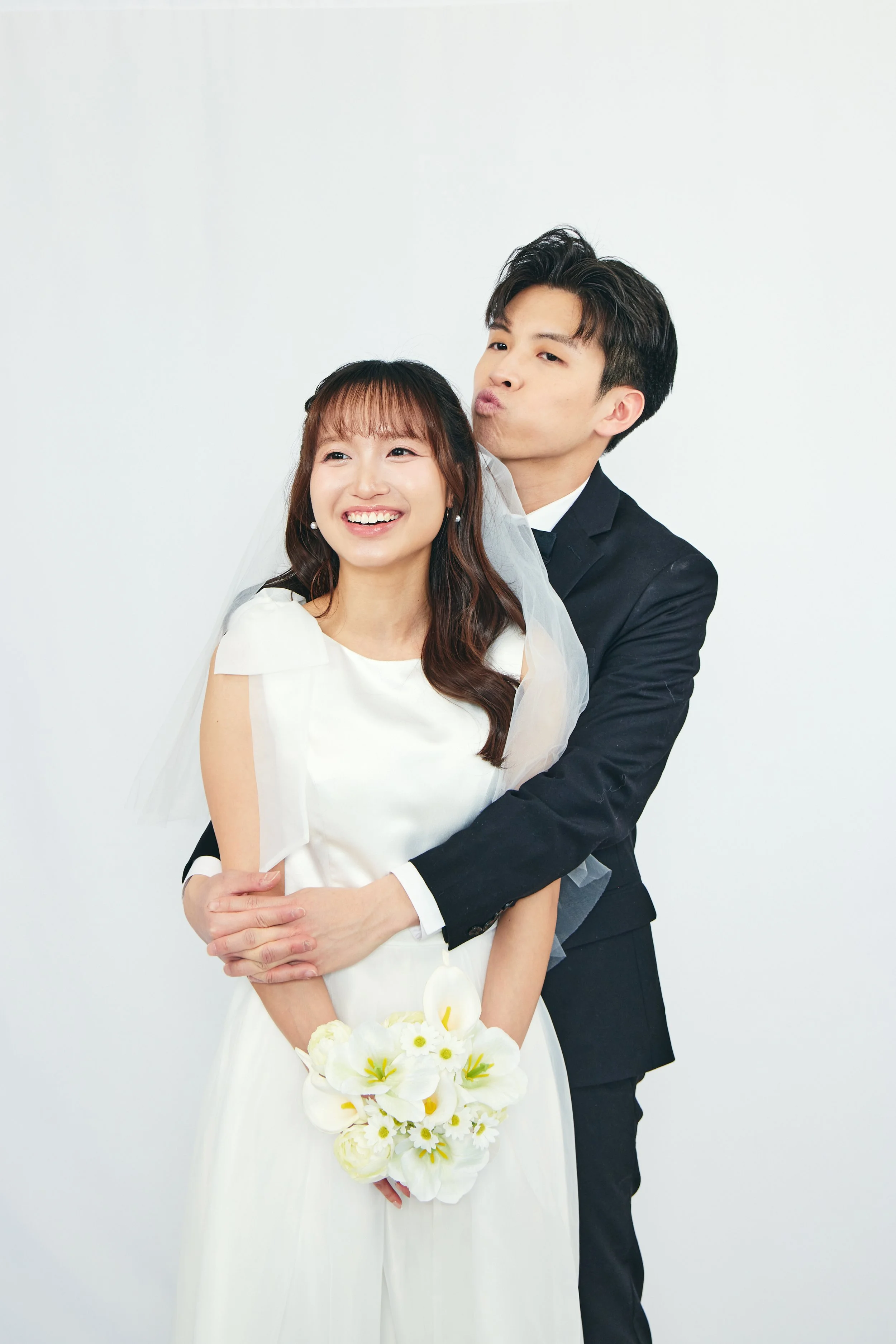 A happy bride and groom in wedding attire posing together against a plain white background.