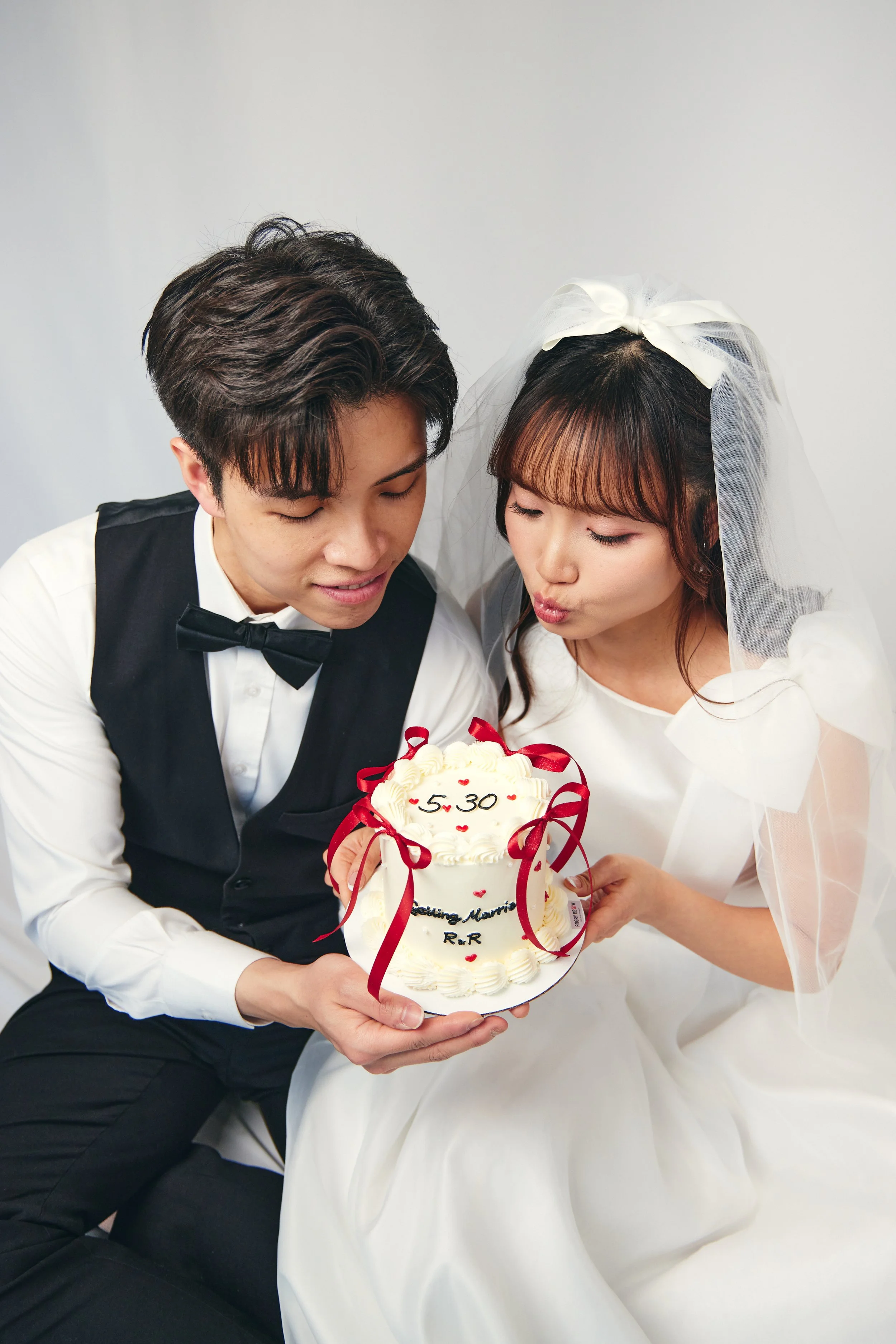A bride and groom in wedding attire holding a wedding cake with the date 5-30 and the words 'Marrying Memoir R&R' on it.