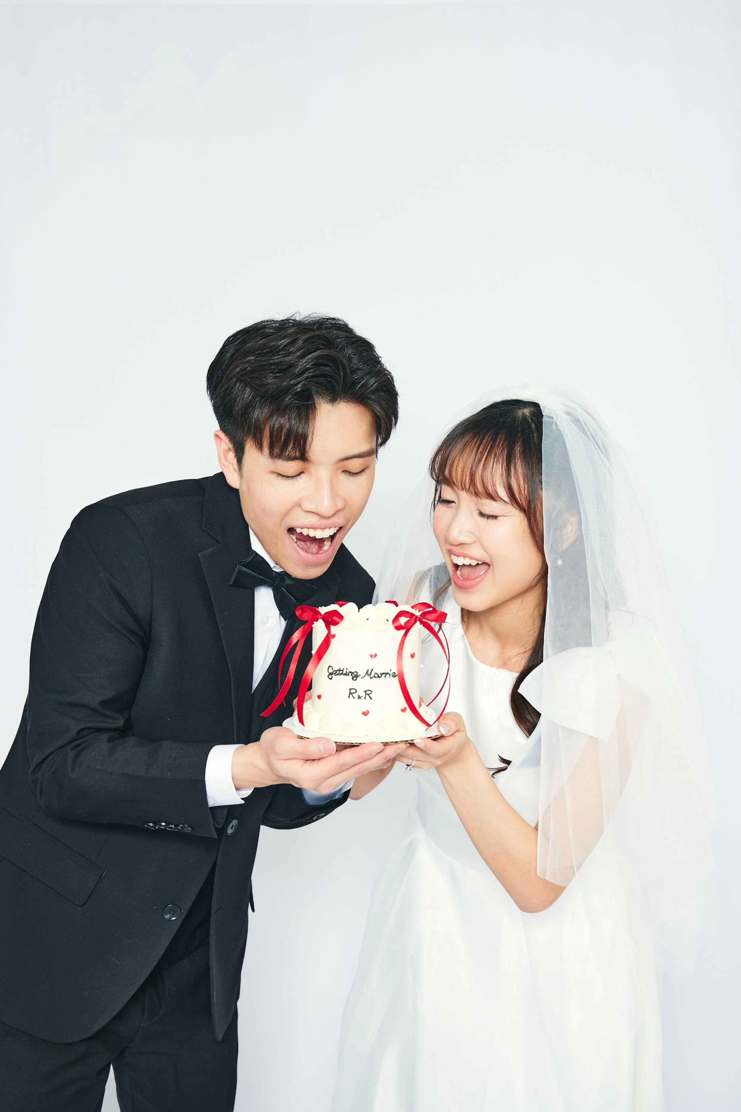 A newlywed couple in wedding attire is holding a wedding cake together and celebrating.