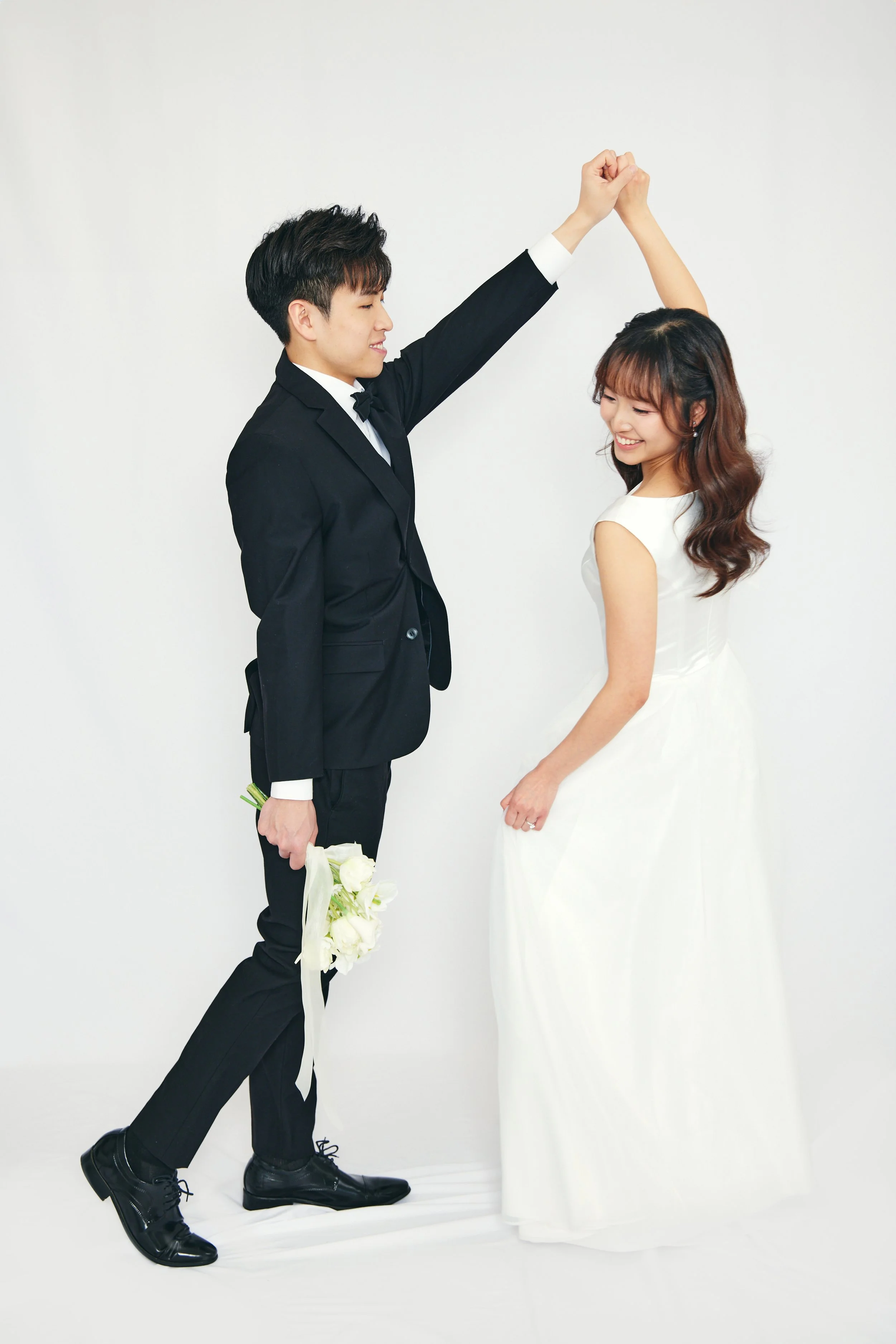 A couple in wedding attire dancing happily, with the groom holding a bouquet of white flowers.