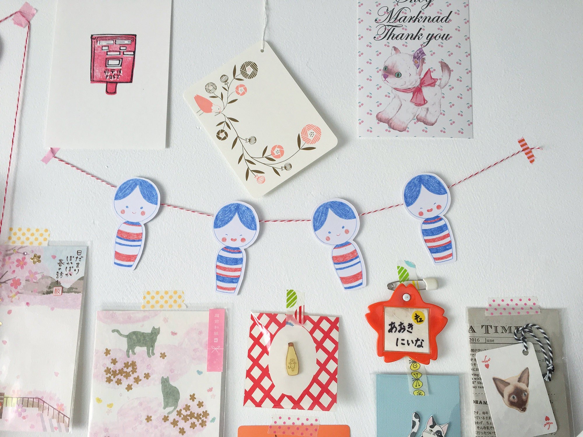 Die cut kokeshi doll note cards strung together like bunting and displayed on a wall with other cute papers