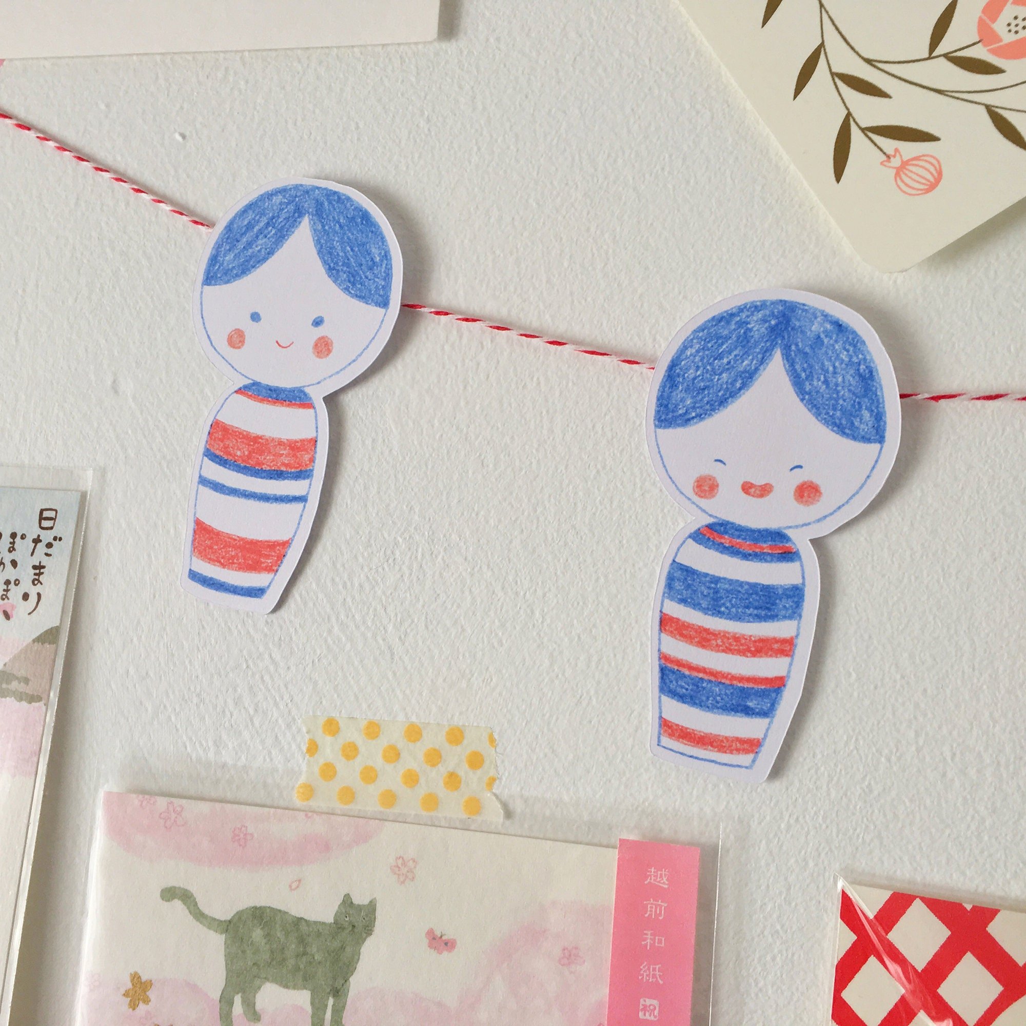 Die cut kokeshi doll note cards strung together like bunting and displayed on a wall with other cute papers