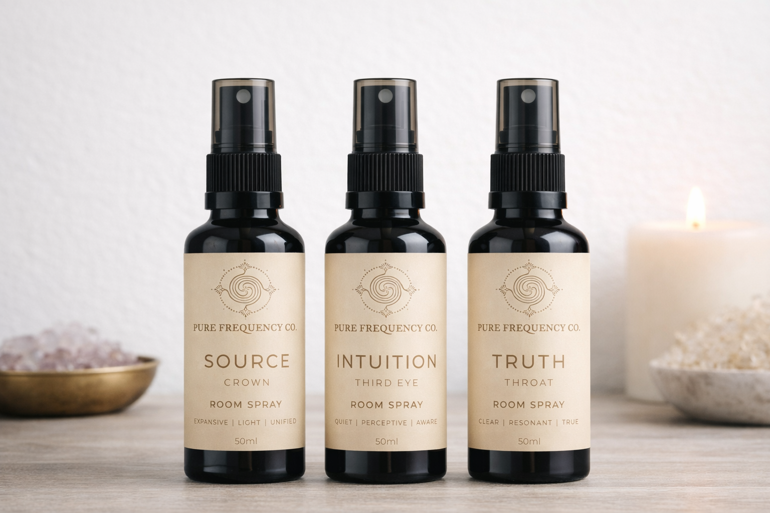 Three black bottles of Pure Frequency Co. room spray with cream labels labeled Source, Intuition, and Truth, placed on a light wooden surface with a bowl of pink salt and a white candle in the background.