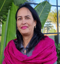 Femme souriante avec un châle rose devant des plantes vertes.
