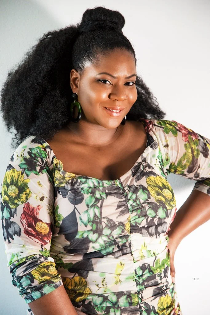 Une femme souriante portant une robe à motifs floraux colorés.